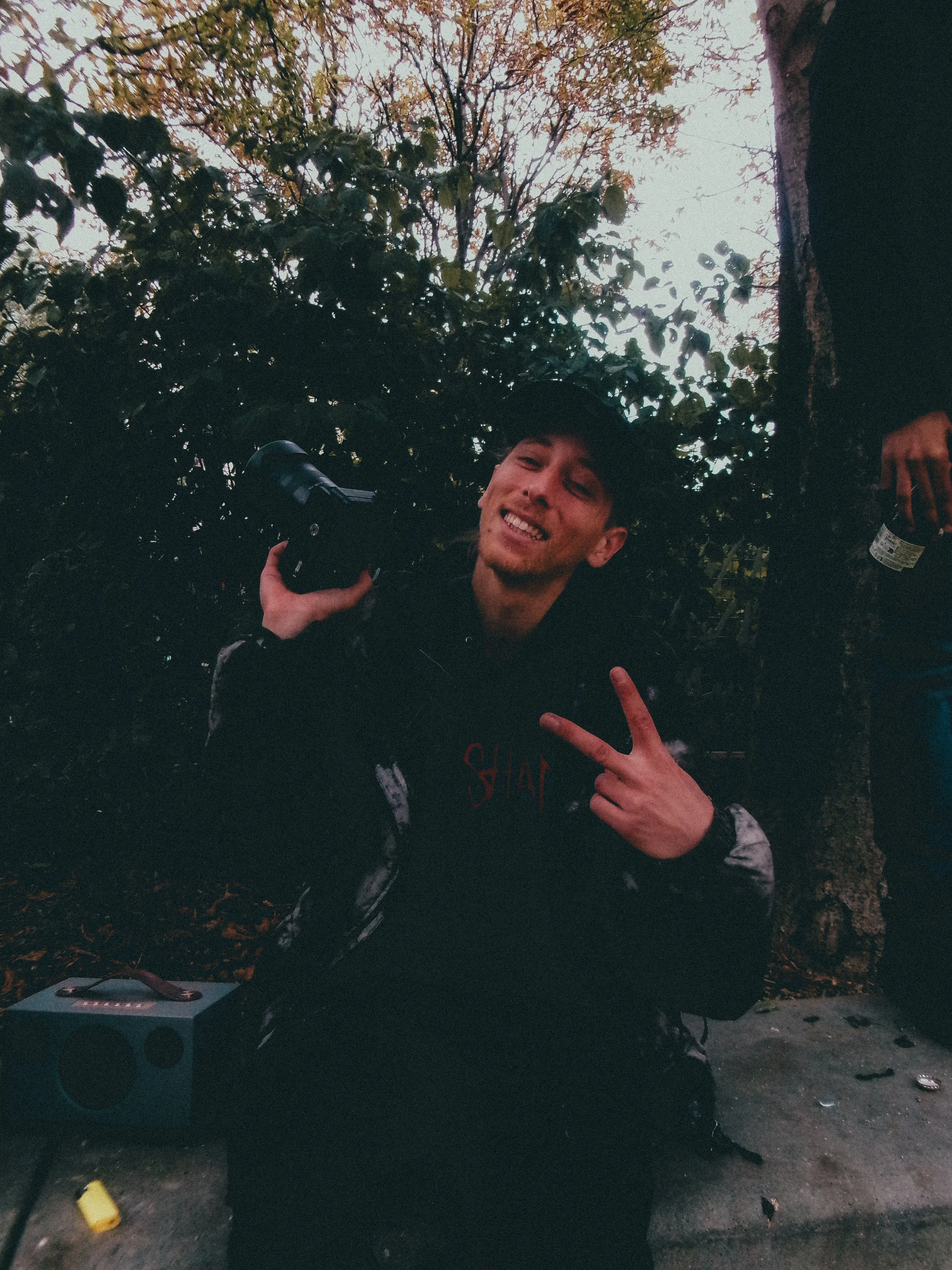 Une personne souriante pose avec un signe de paix devant des arbres.