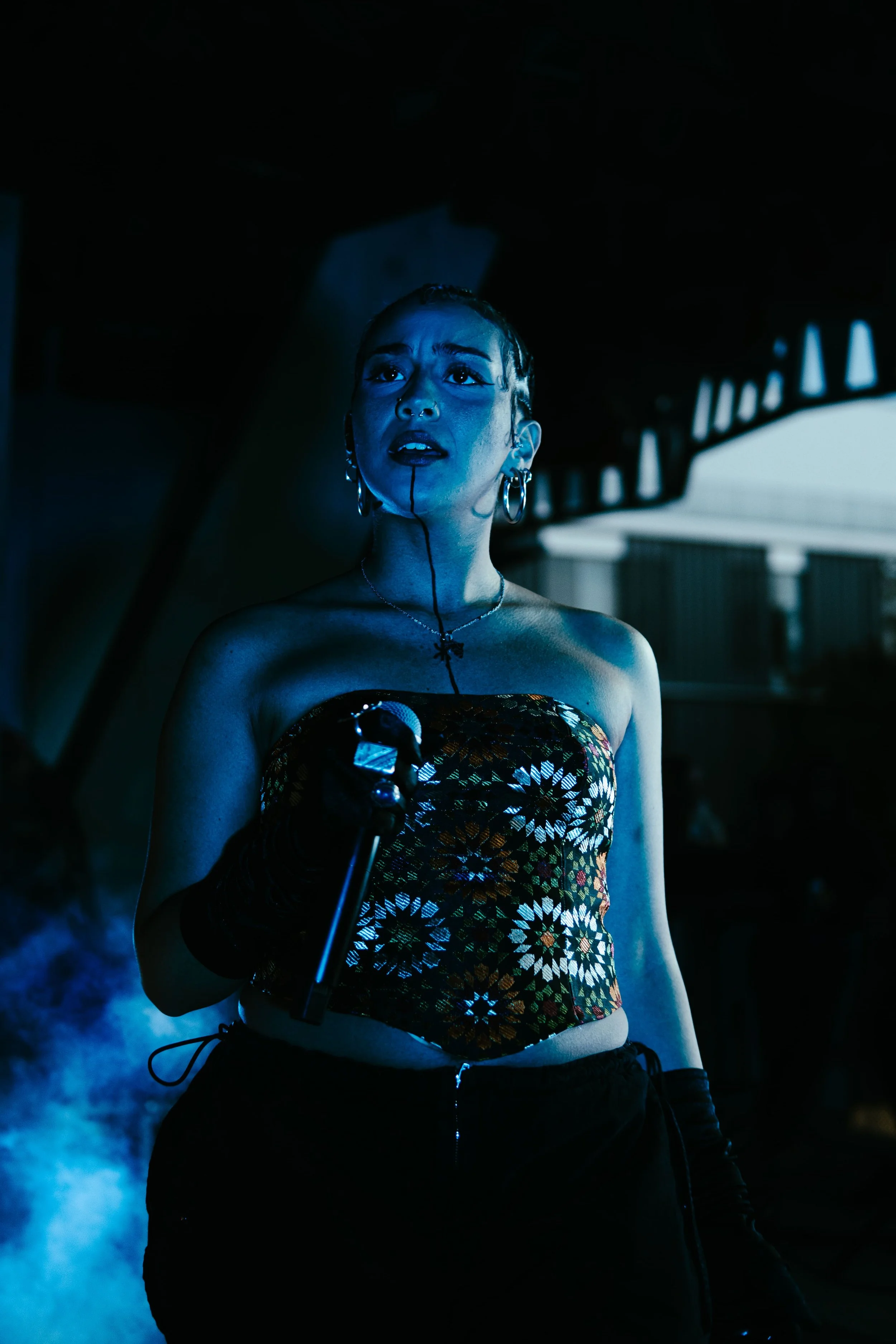 Une femme chante ou parle avec un microphone dans un environnement sombre, avec un éclairage bleu.