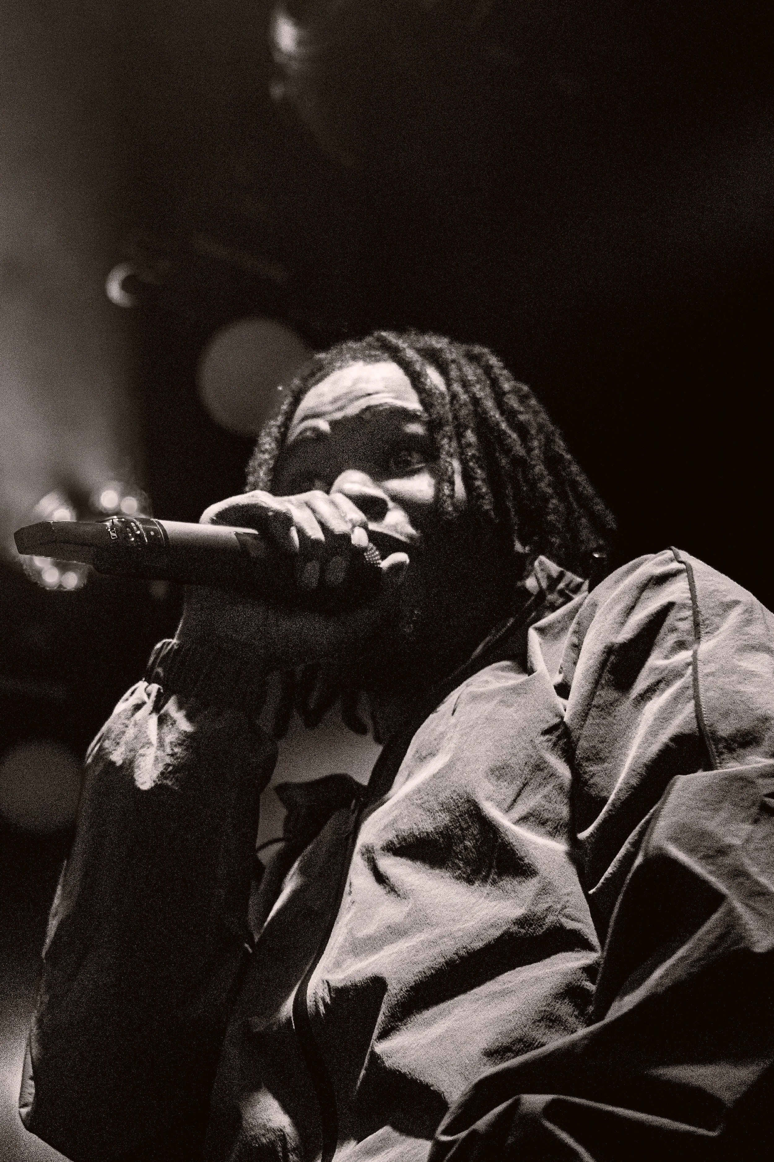 Un artiste avec des dreadlocks tient un microphone lors d'une performance, en noir et blanc.