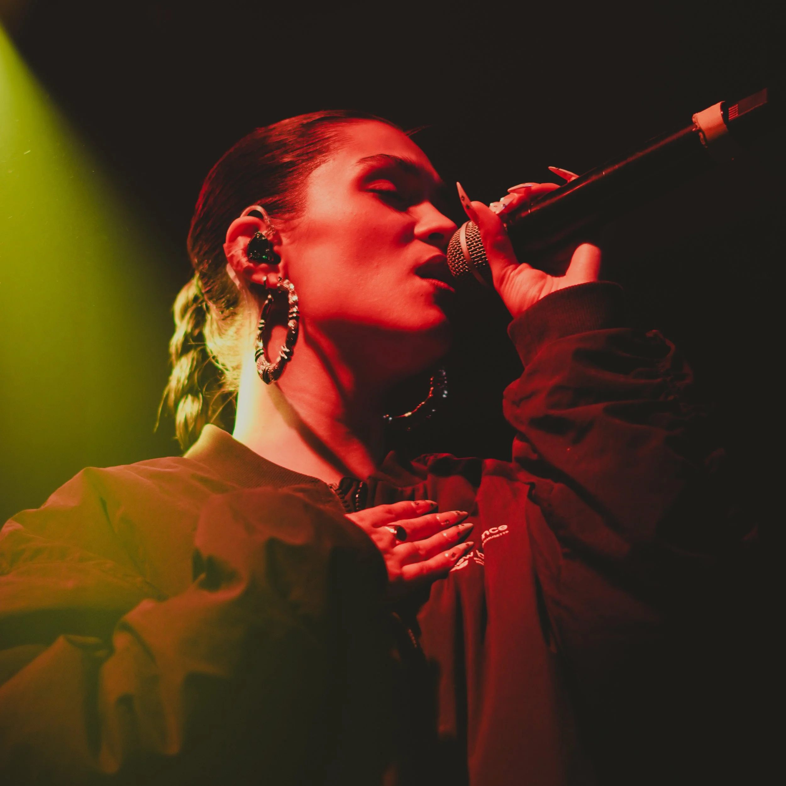 Une femme chante dans un micro lors d'une performance, éclairée par un éclairage coloré.