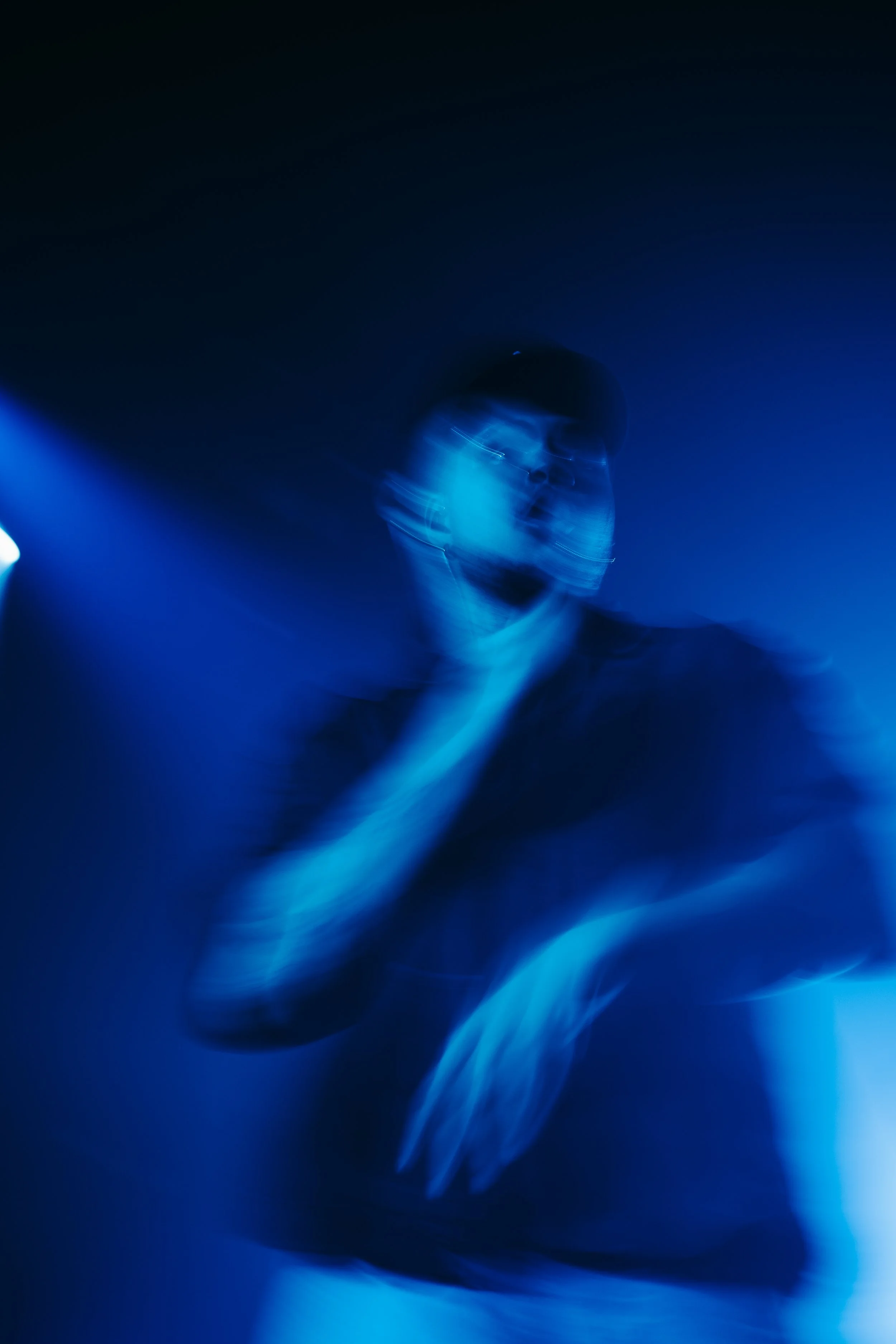 Personne portant un masque dans une lumière bleue, avec un effet de flou et de mouvement.