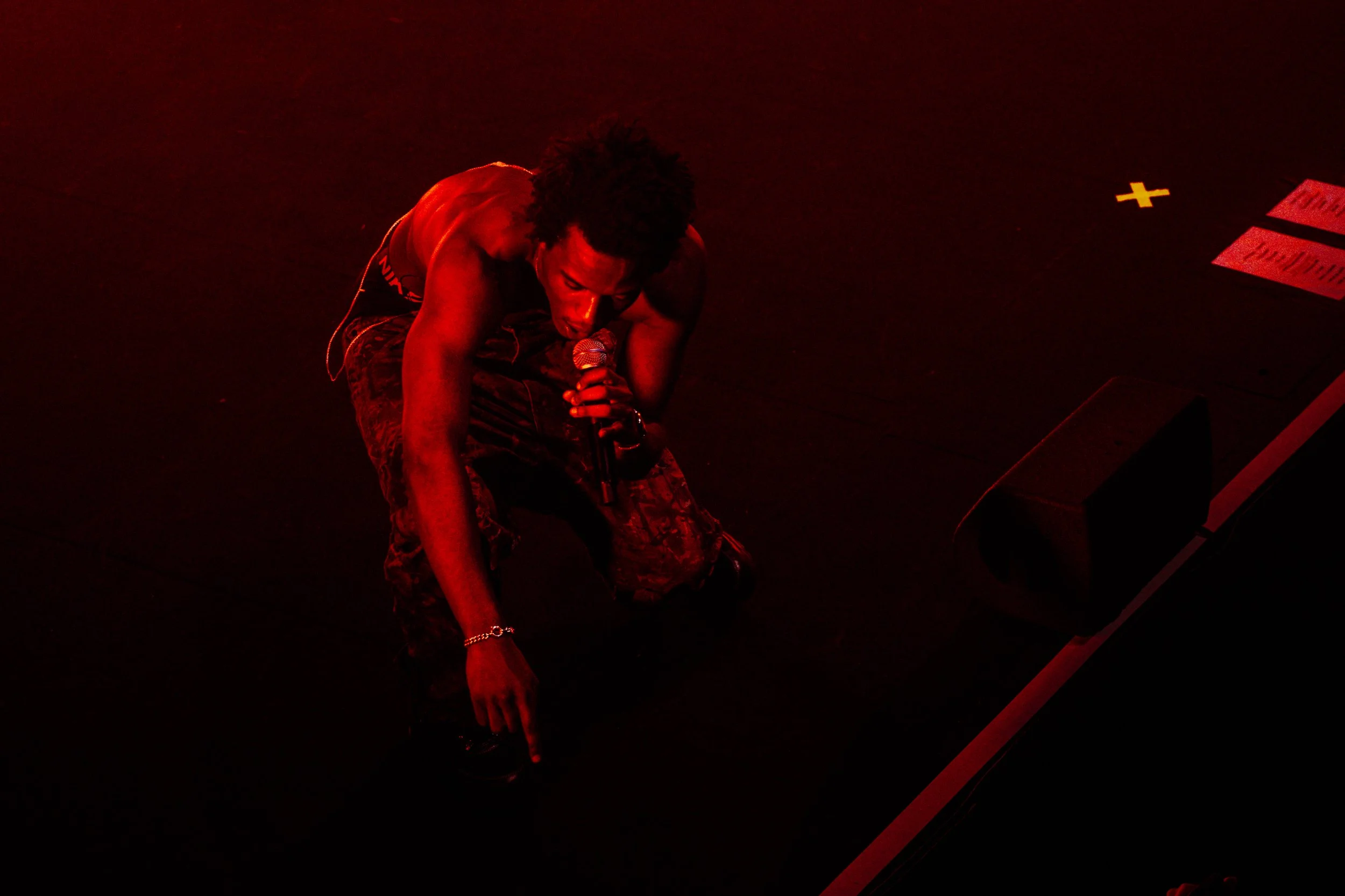 Un artiste chanteur à genoux sur scène, tenant un microphone, dans une lumière rouge intense.
