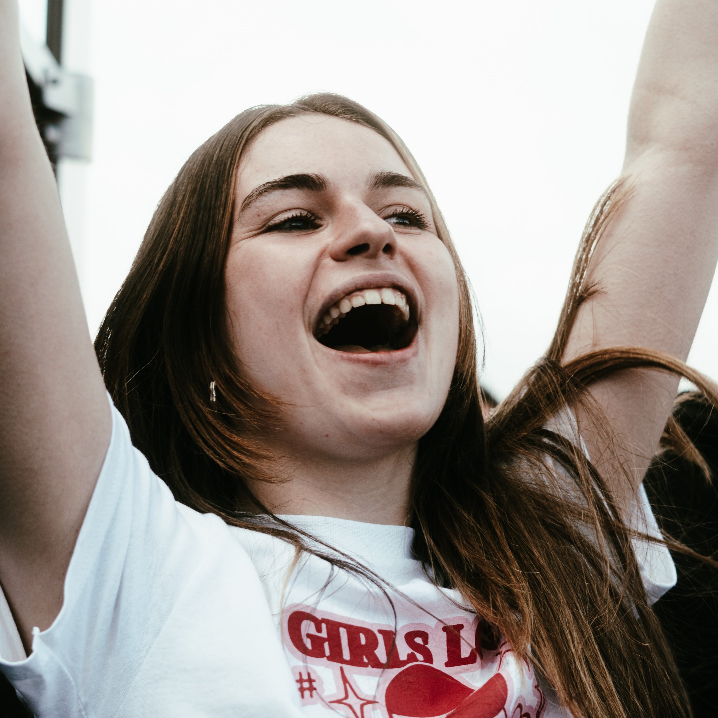 Une jeune femme avec les bras levés, souriante et criant de joie, portant un t-shirt blanc à motif rouge.