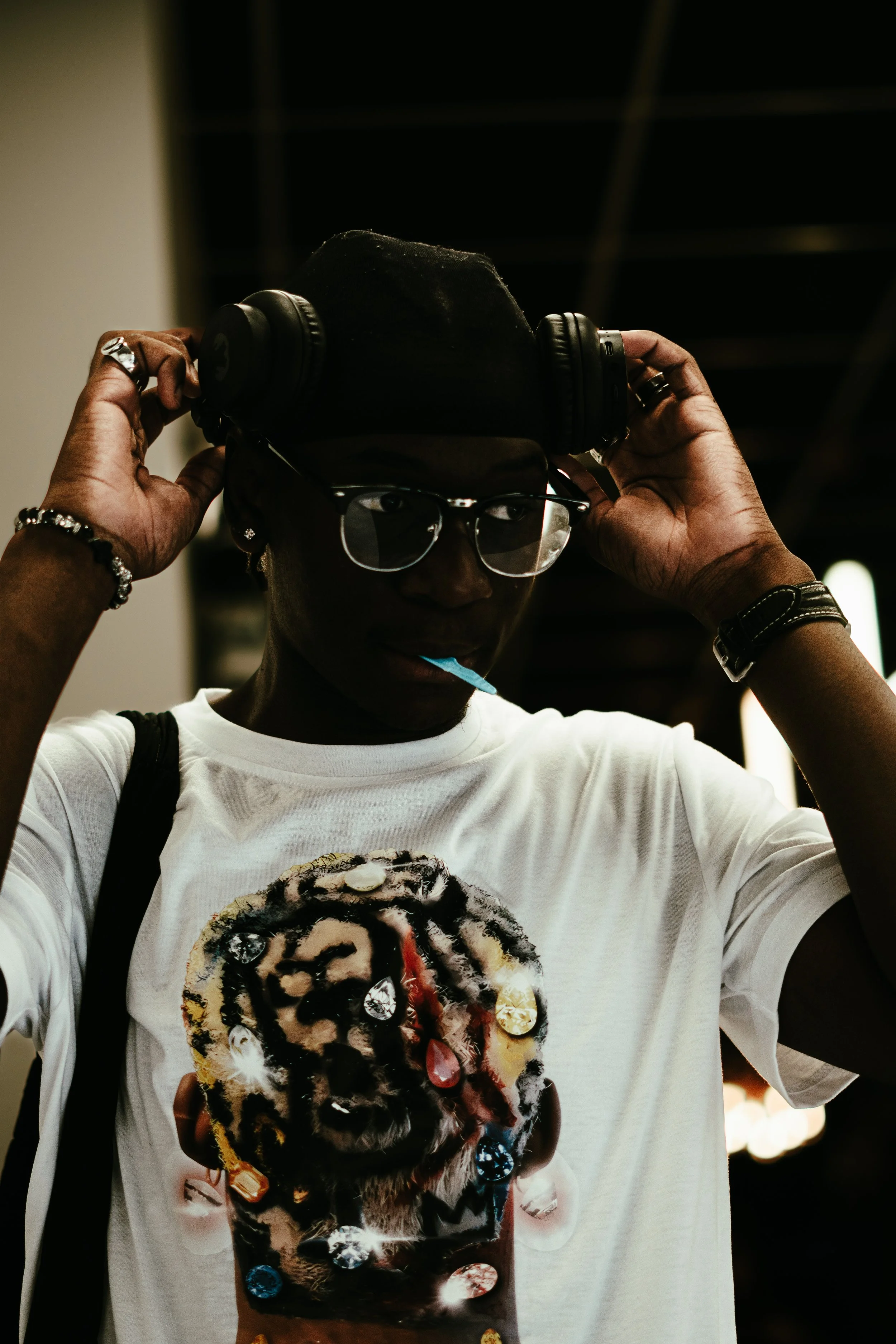 Une jeune personne portant des lunettes, un t-shirt blanc avec une image d'une tête de bébé en relief et ornée de pierres précieuses, ajuste un casque audio noir sur sa tête.