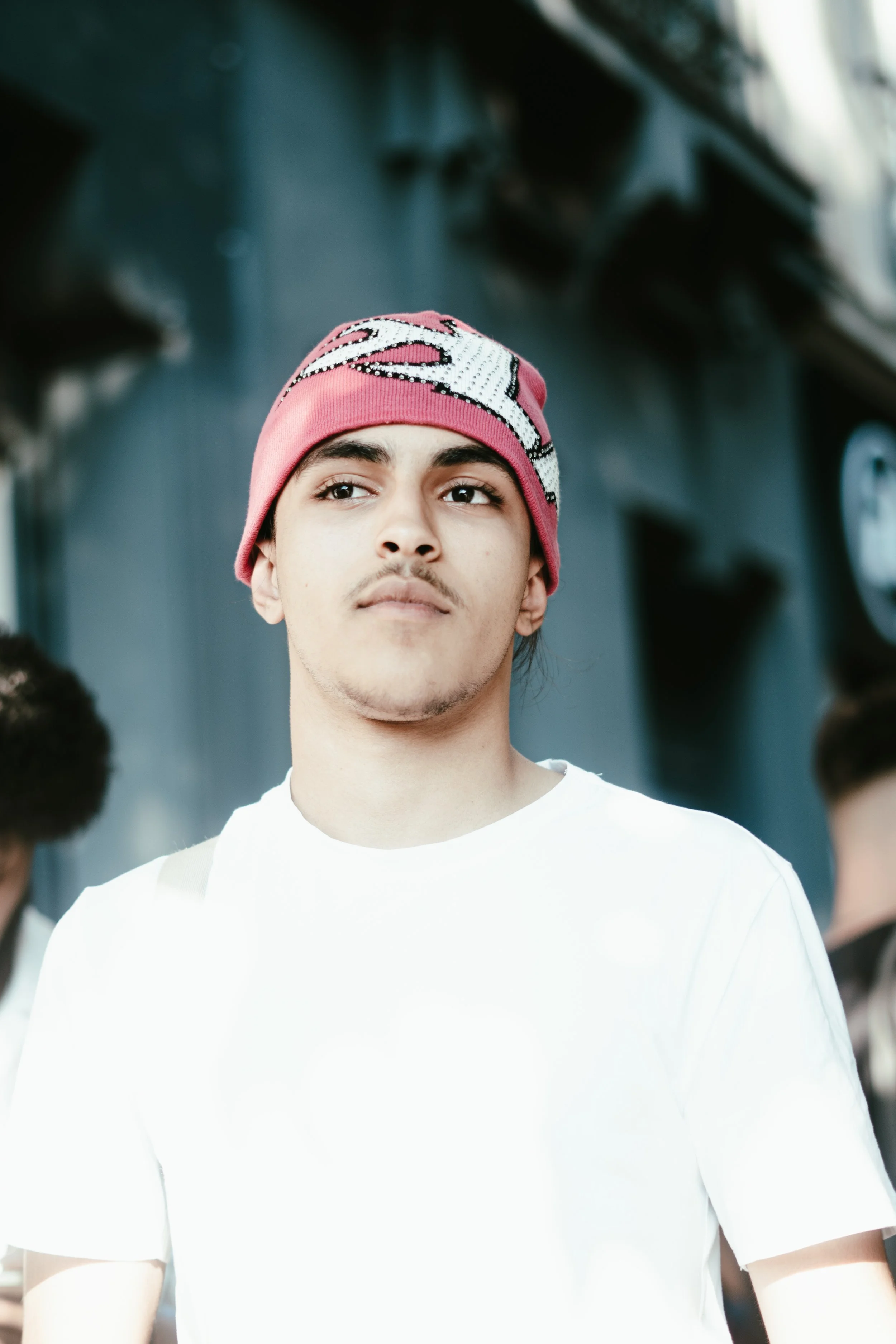 Jeune homme portant un bonnet rose et blanc, vêtu d'un T-shirt blanc, dans une ambiance urbaine.