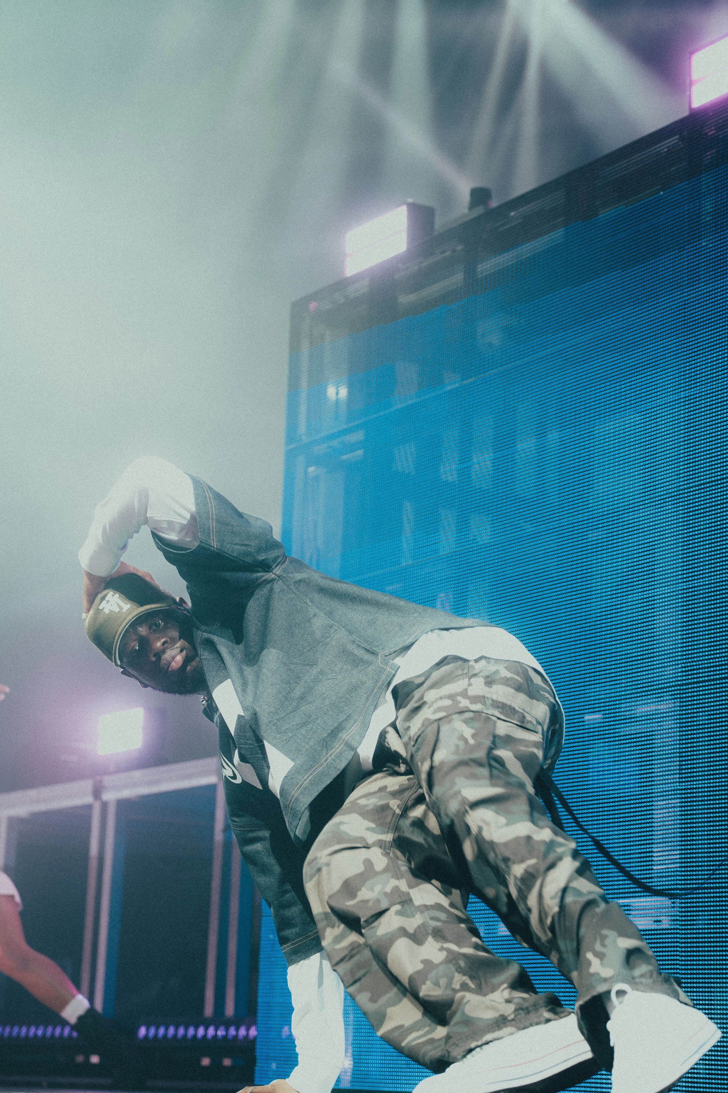 Un danseur en tenue urbaine à un spectacle de danse urbaine sur scène avec un grand écran lumineux en arrière-plan.