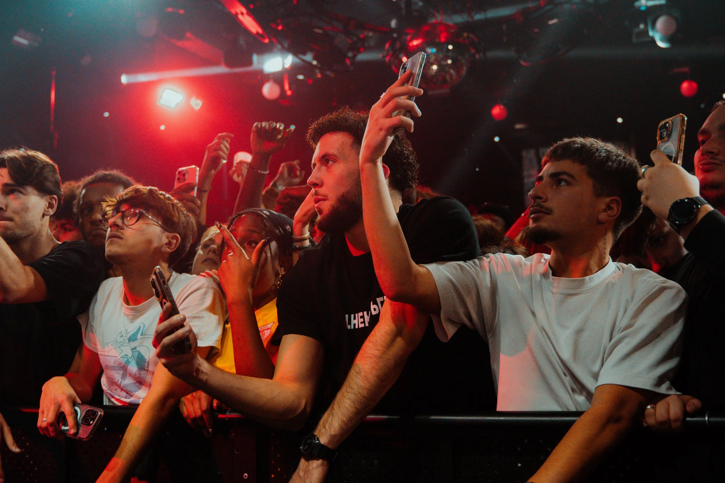 Public attentif lors d'un concert ou d'un événement avec des personnes tenant leur téléphone portable, sous un éclairage rouge