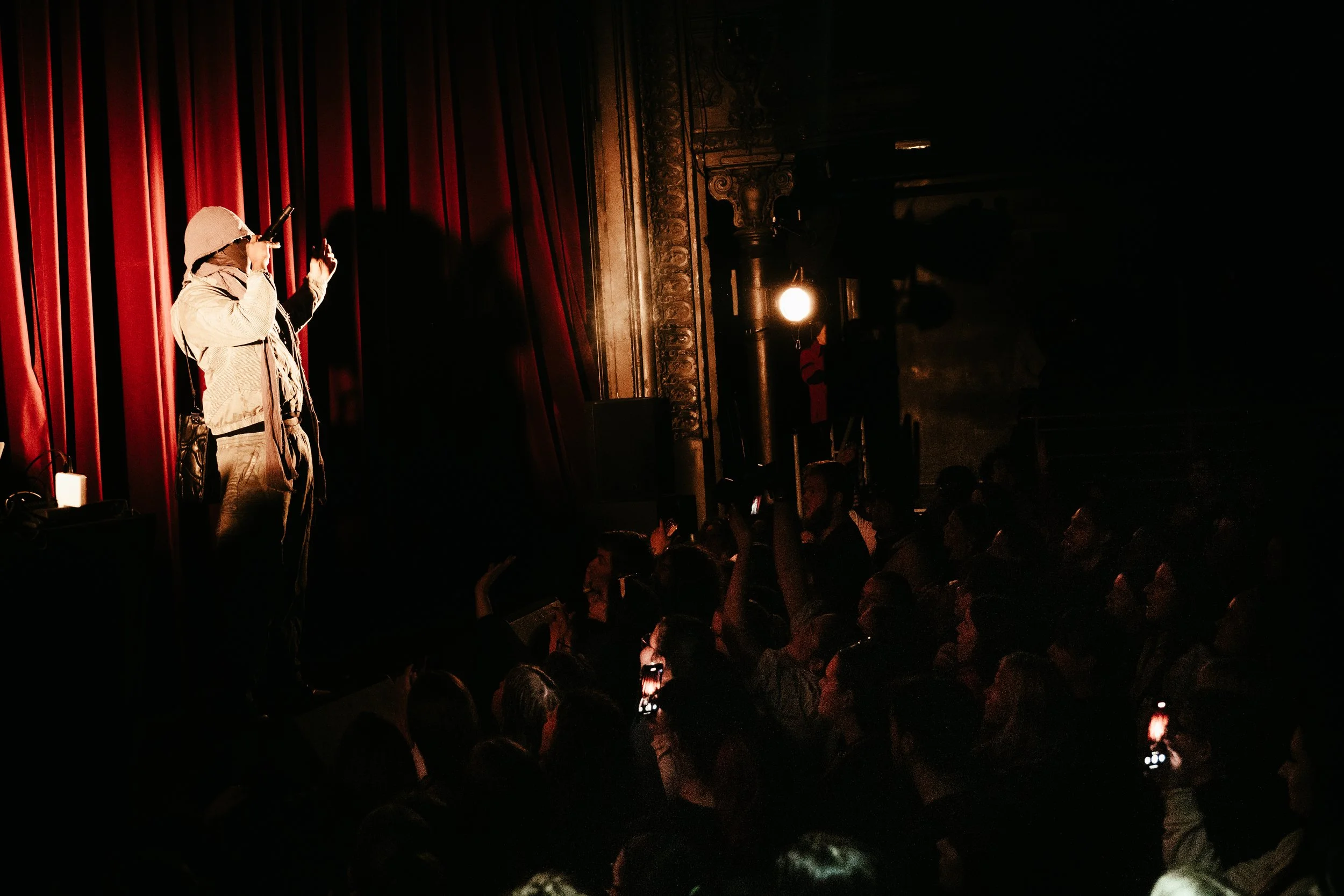 Un artiste de rue joue de la musique devant une grande foule dans une salle sombre avec des rideaux rouges.