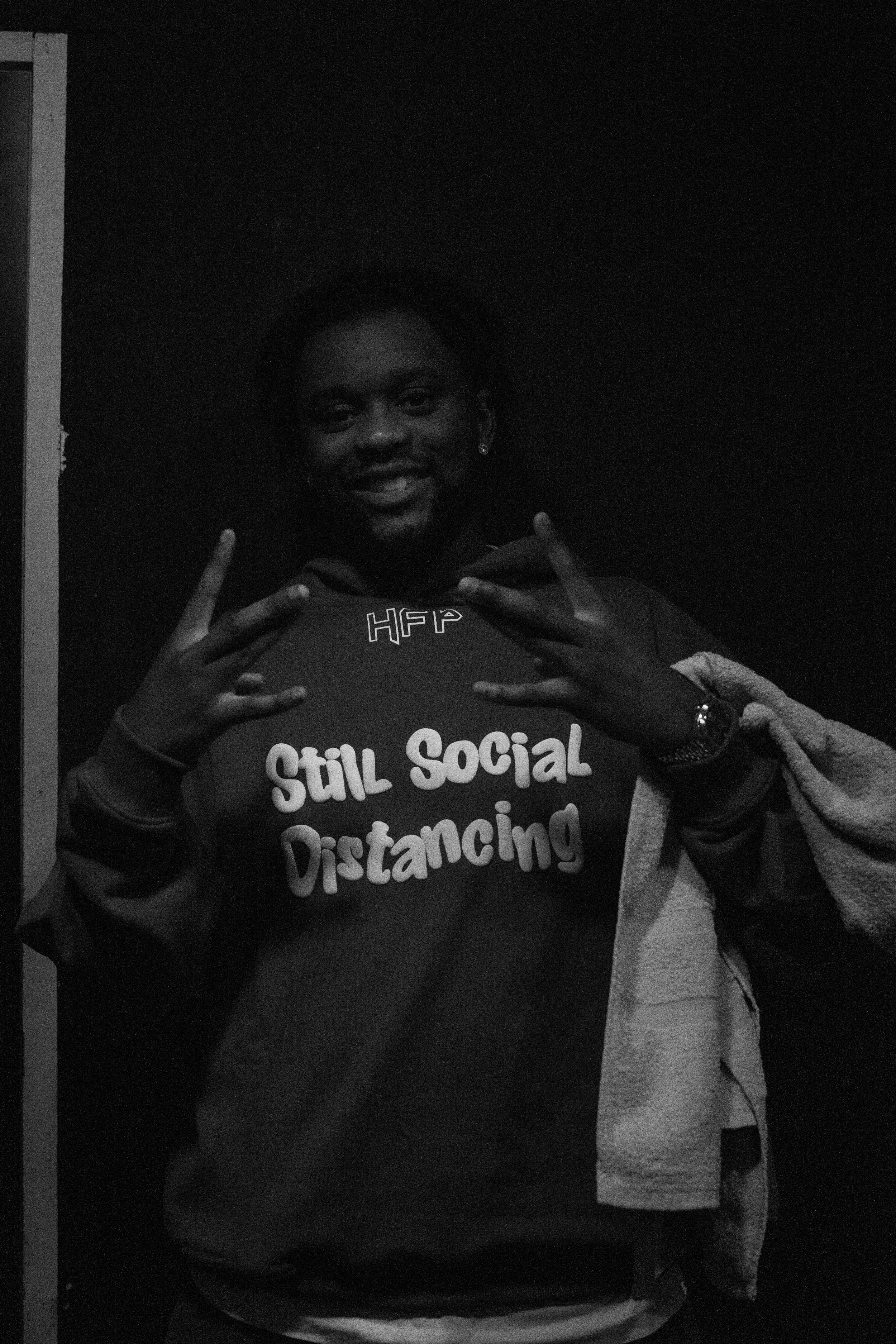 Une femme souriante portant un sweat-shirt avec le texte 'S’il Social Distancing' et faisant des signes de paix avec ses mains.