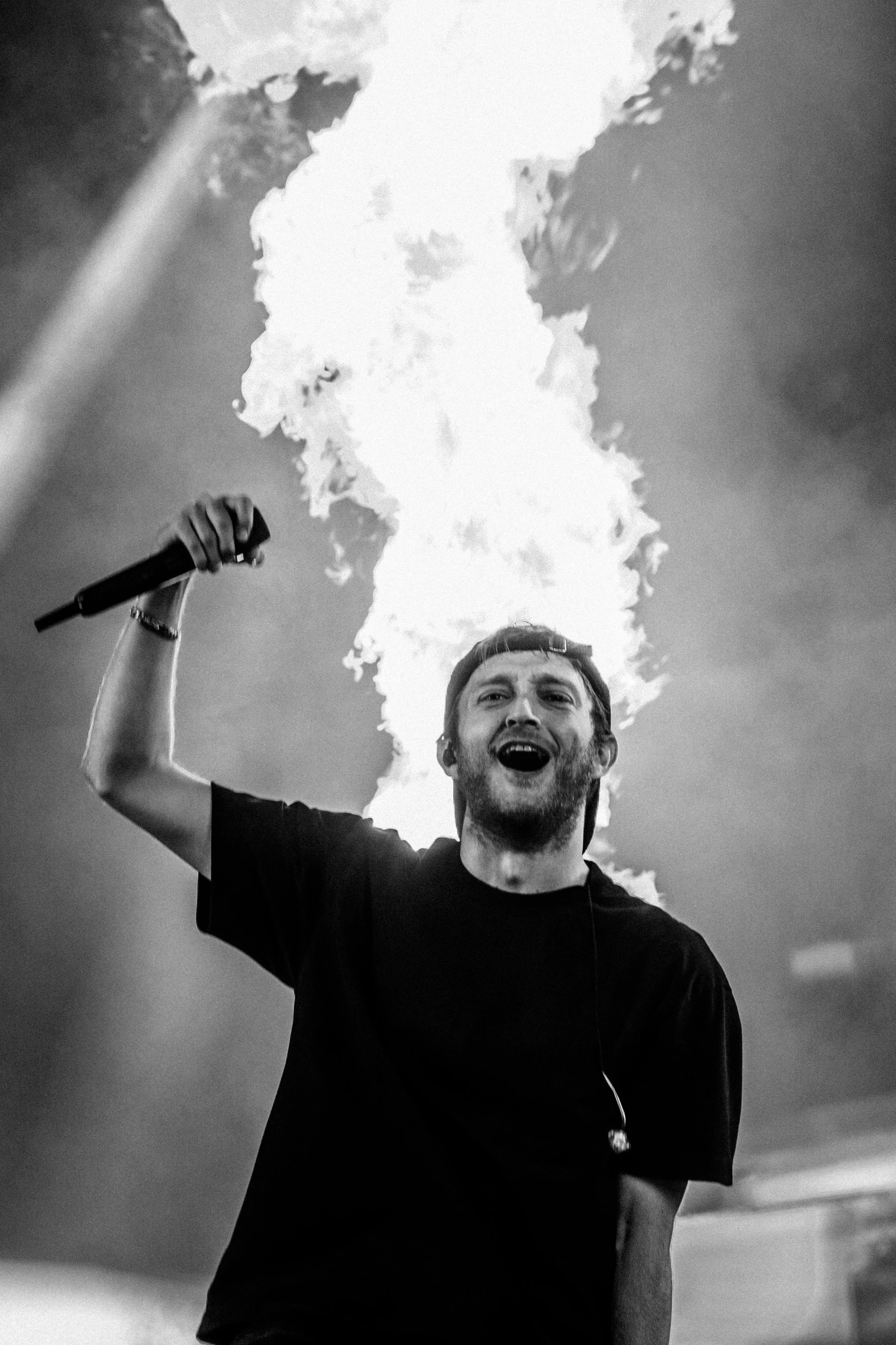 Un homme tenant un microphone avec des flammes derrière lui, en train de chanter ou de crier lors d'un concert.
