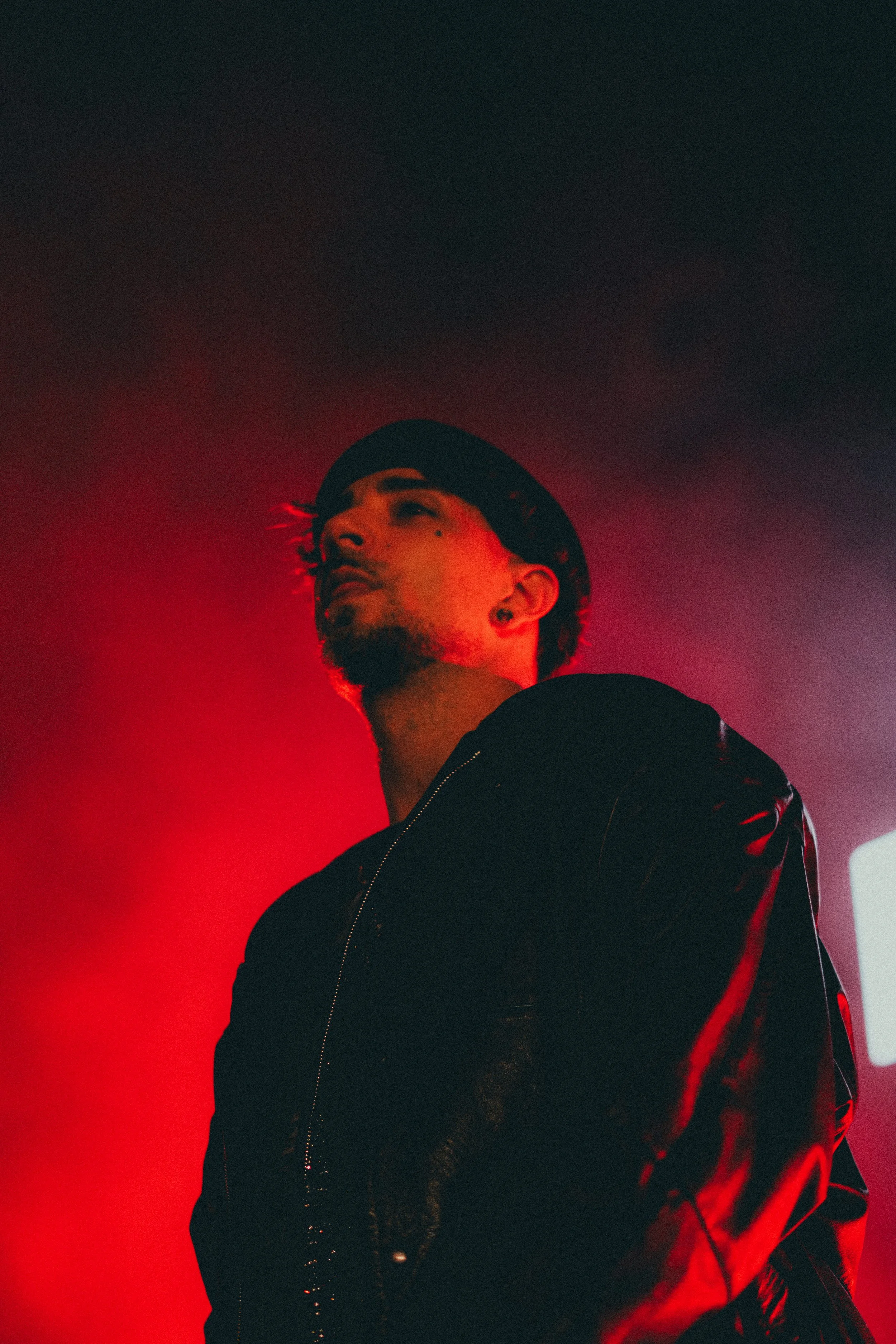 Jeune homme avec un chapeau noir, veste en cuir, sous un éclairage rouge