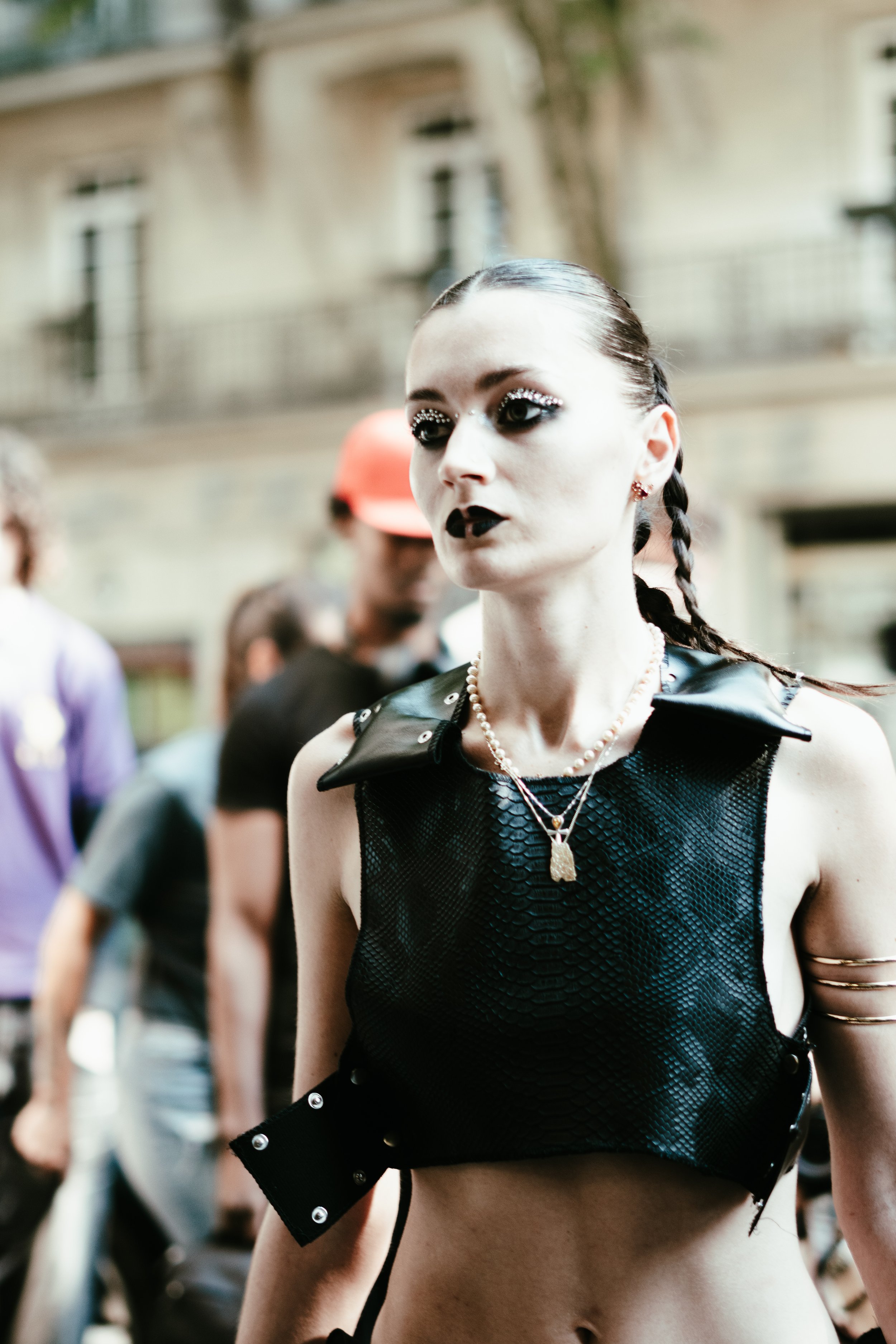 Jeune femme avec maquillage gothique, vêtements en cuir noir et accessoires, manucure noire, dans une foule en plein air.