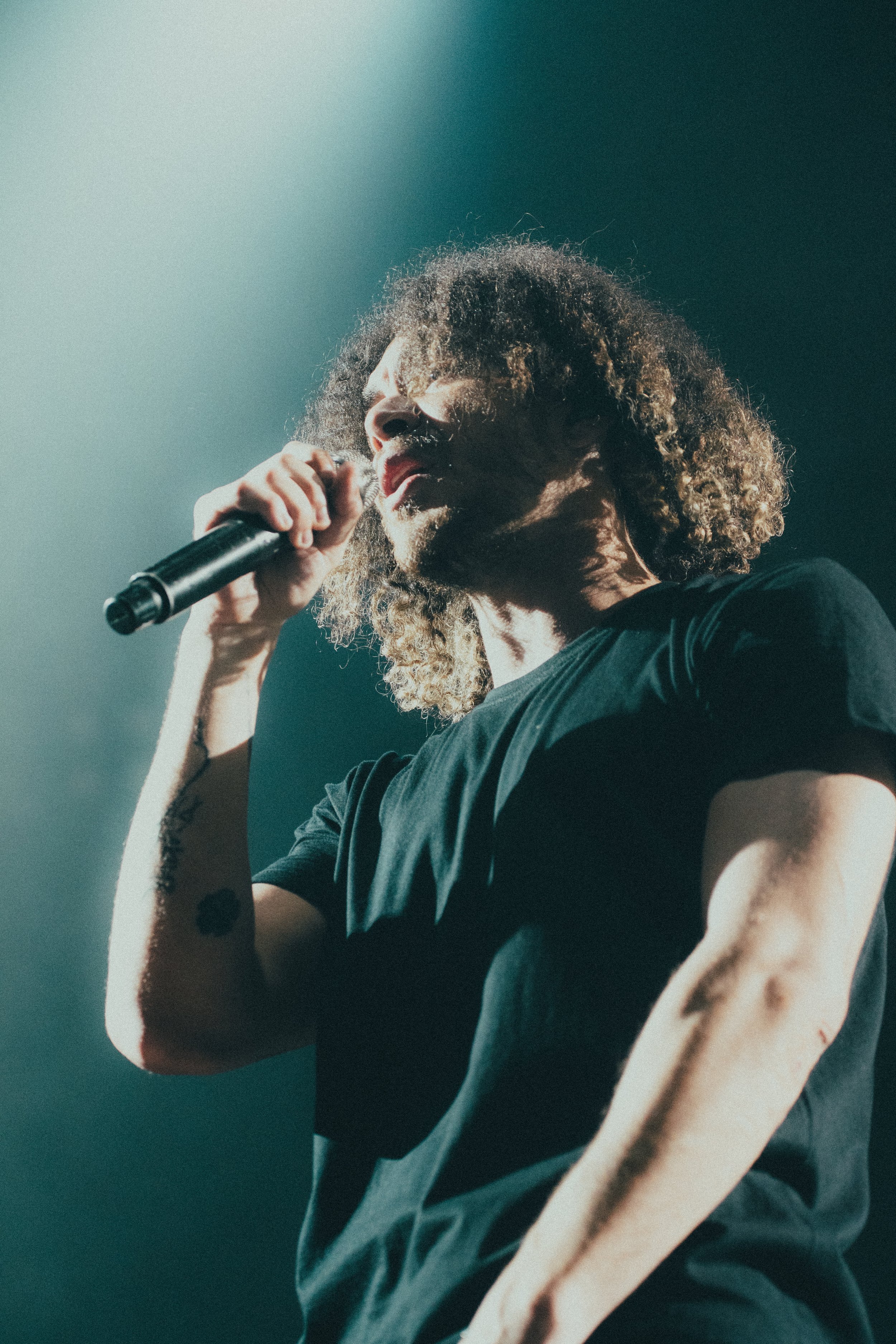 Une personne avec des cheveux bouclés, tenant un microphone au cours d'une performance ou d'un concert.