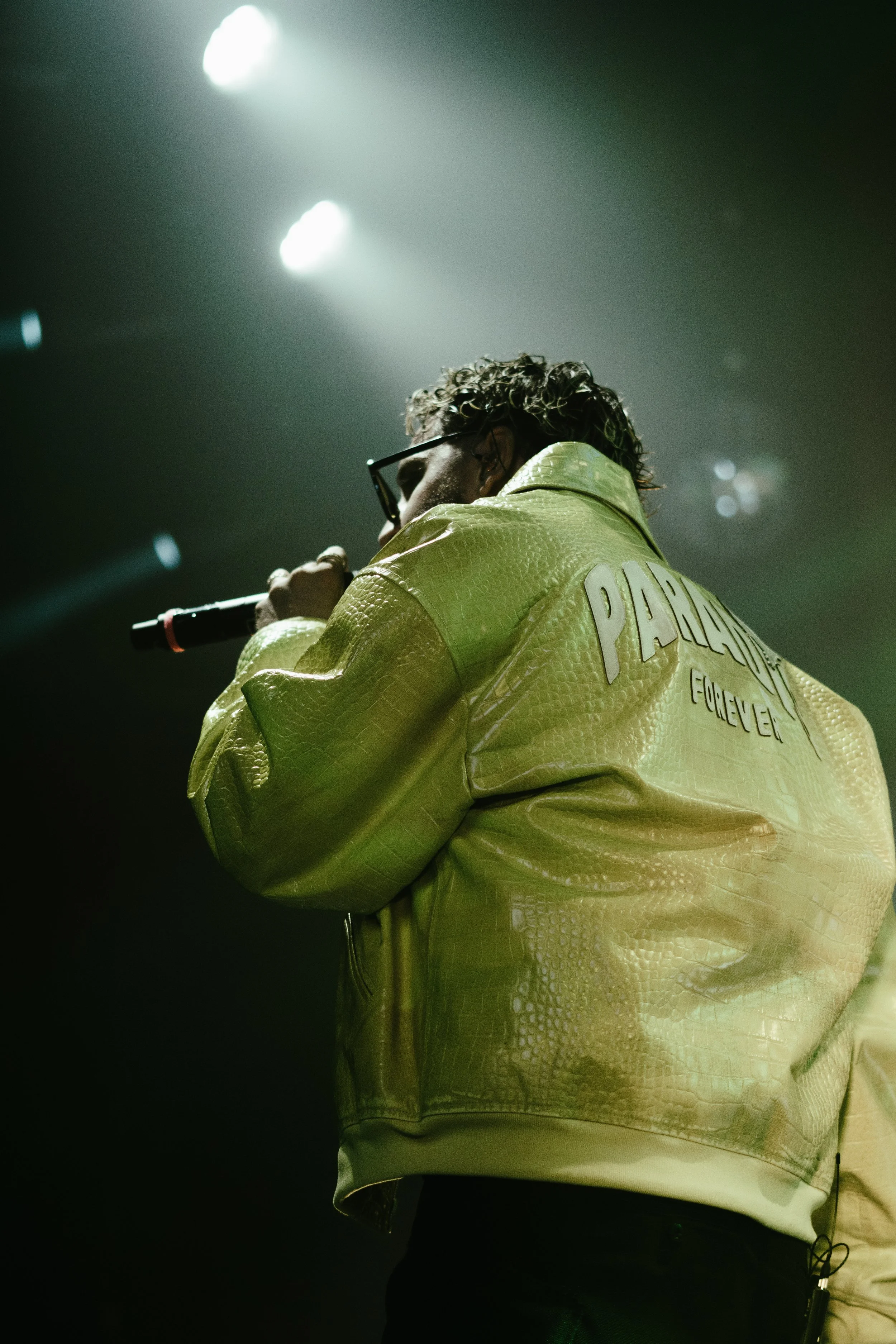 Un artiste portant une veste jaune avec le nom 'PABLO' et tenant un microphone sur scène.