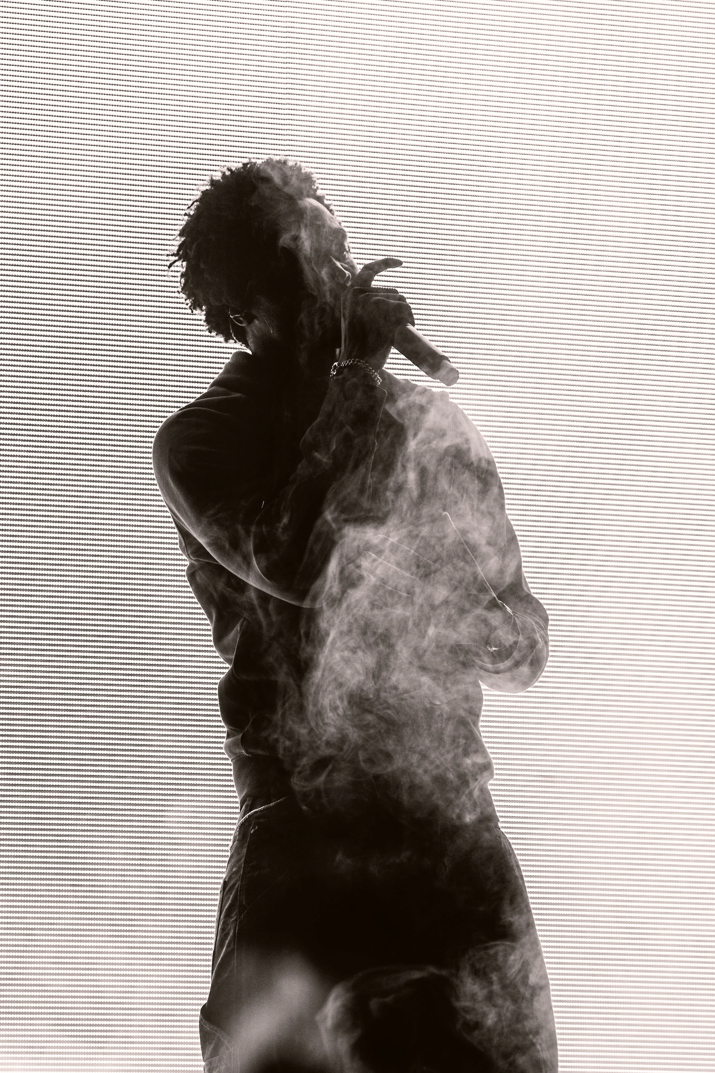 Un homme en silhouette fumant une cigarette ou un cigarillo, avec un écran lumineux en arrière-plan.