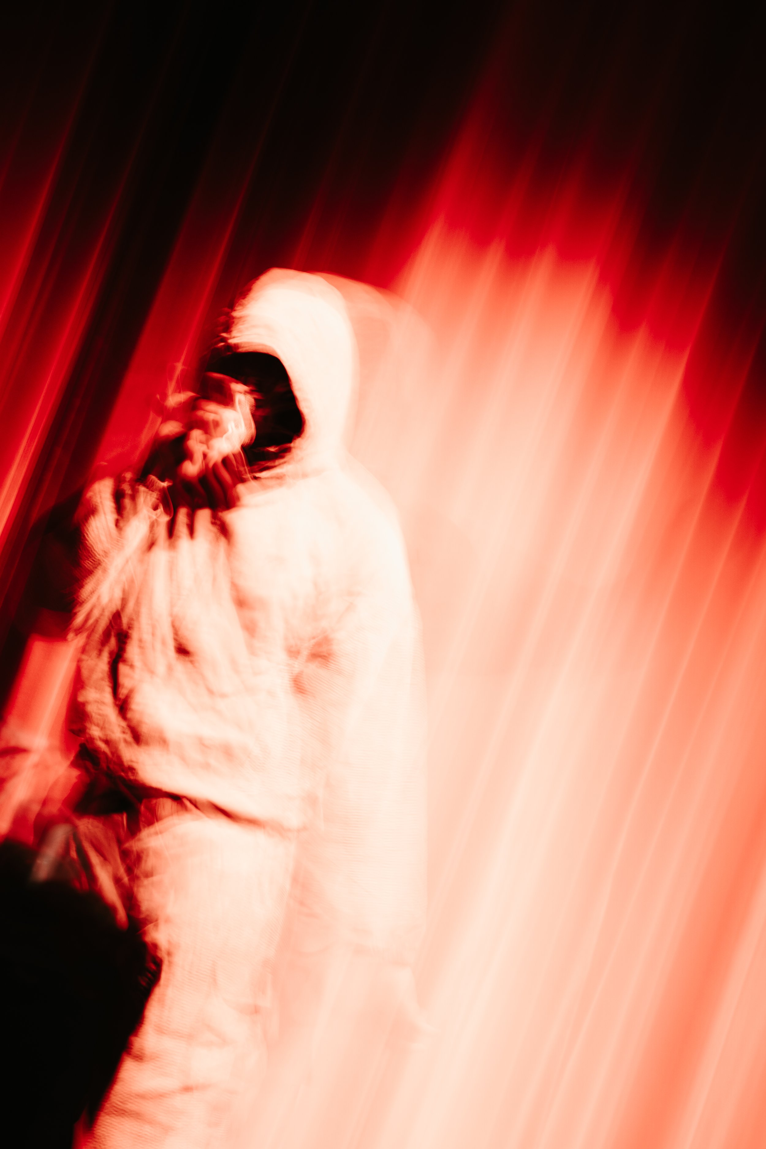 Une personne portant une veste blanche avec une capuche, utilisant un masque facial, vidéo en mouvement avec un effet de flou et de traînée lumineuse rouge et noire.