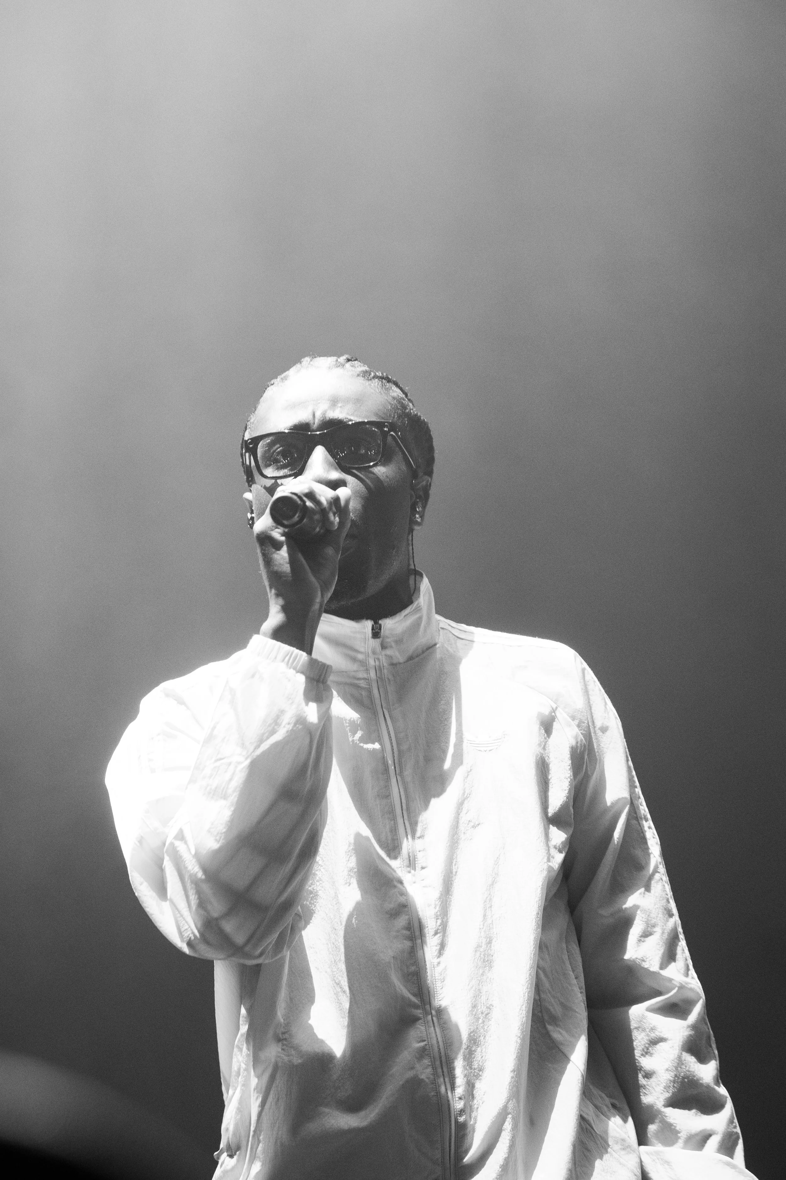 Un homme portant des lunettes et une veste blanche, tenant un microphone, lors d'une performance ou d'un concert.