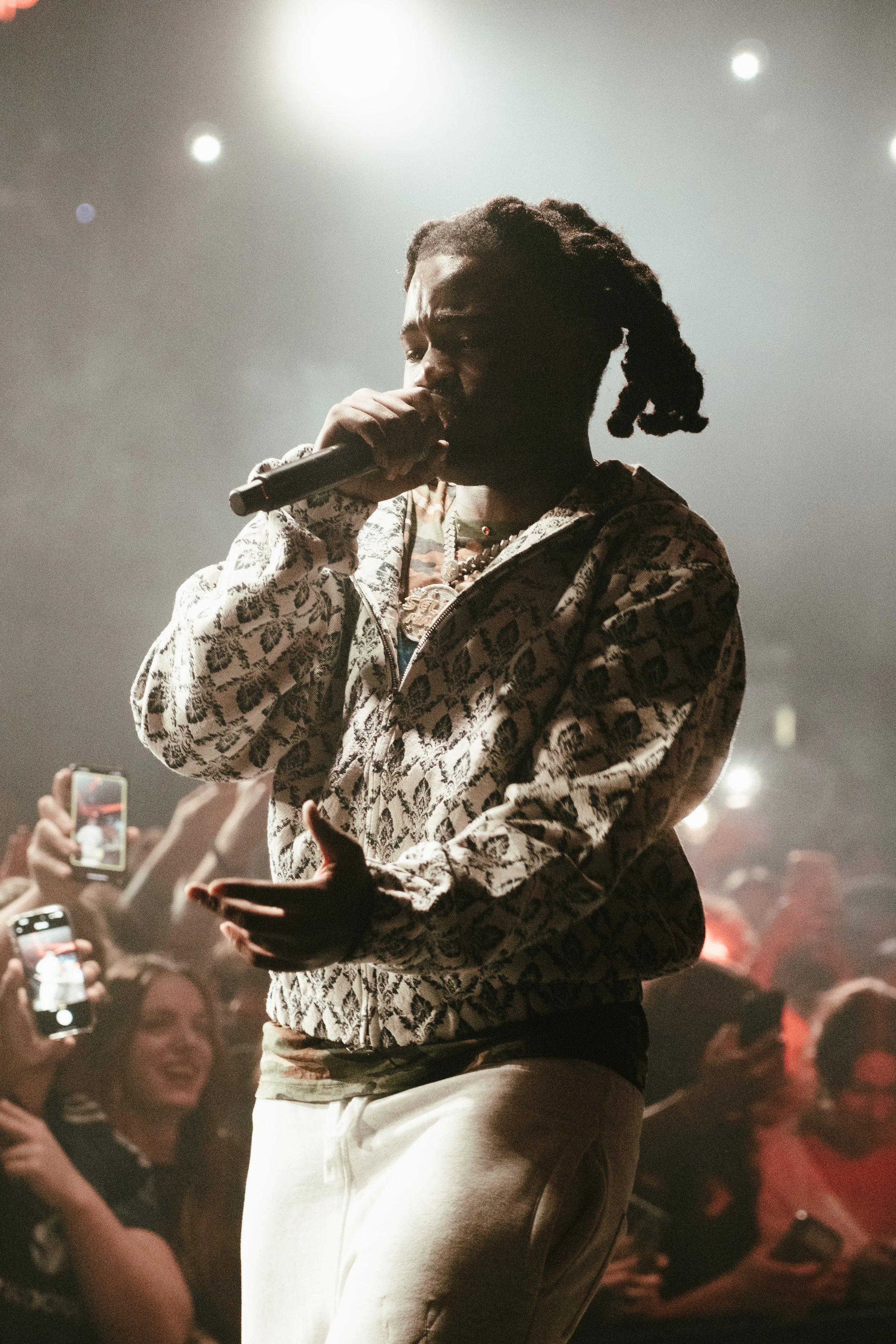 Un artiste de rap performe sur scène devant une foule captivée, sous des lumières de concert.