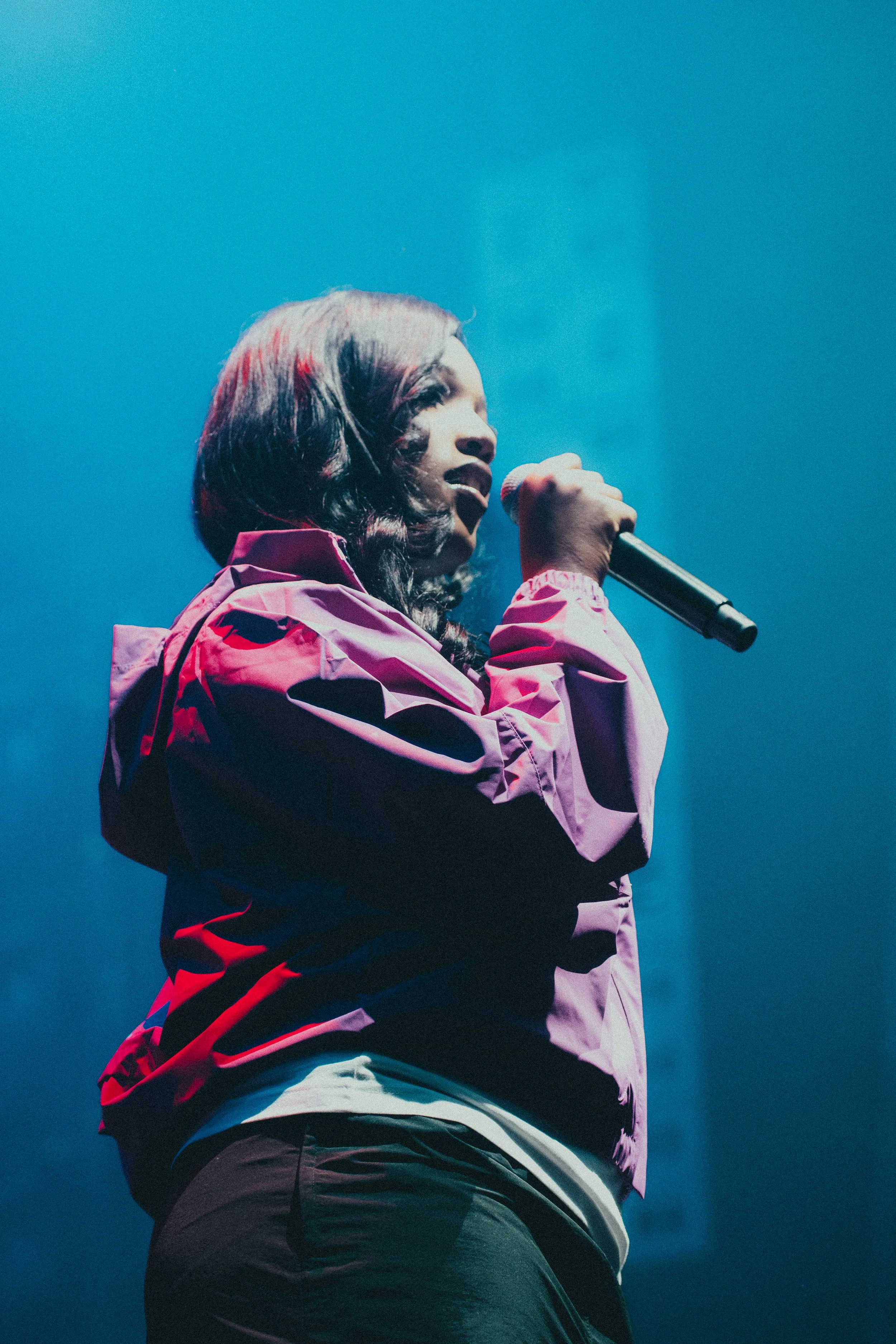Une jeune femme chante dans un micro, éclairée par des lumières bleues, lors d'une performance sur scène.