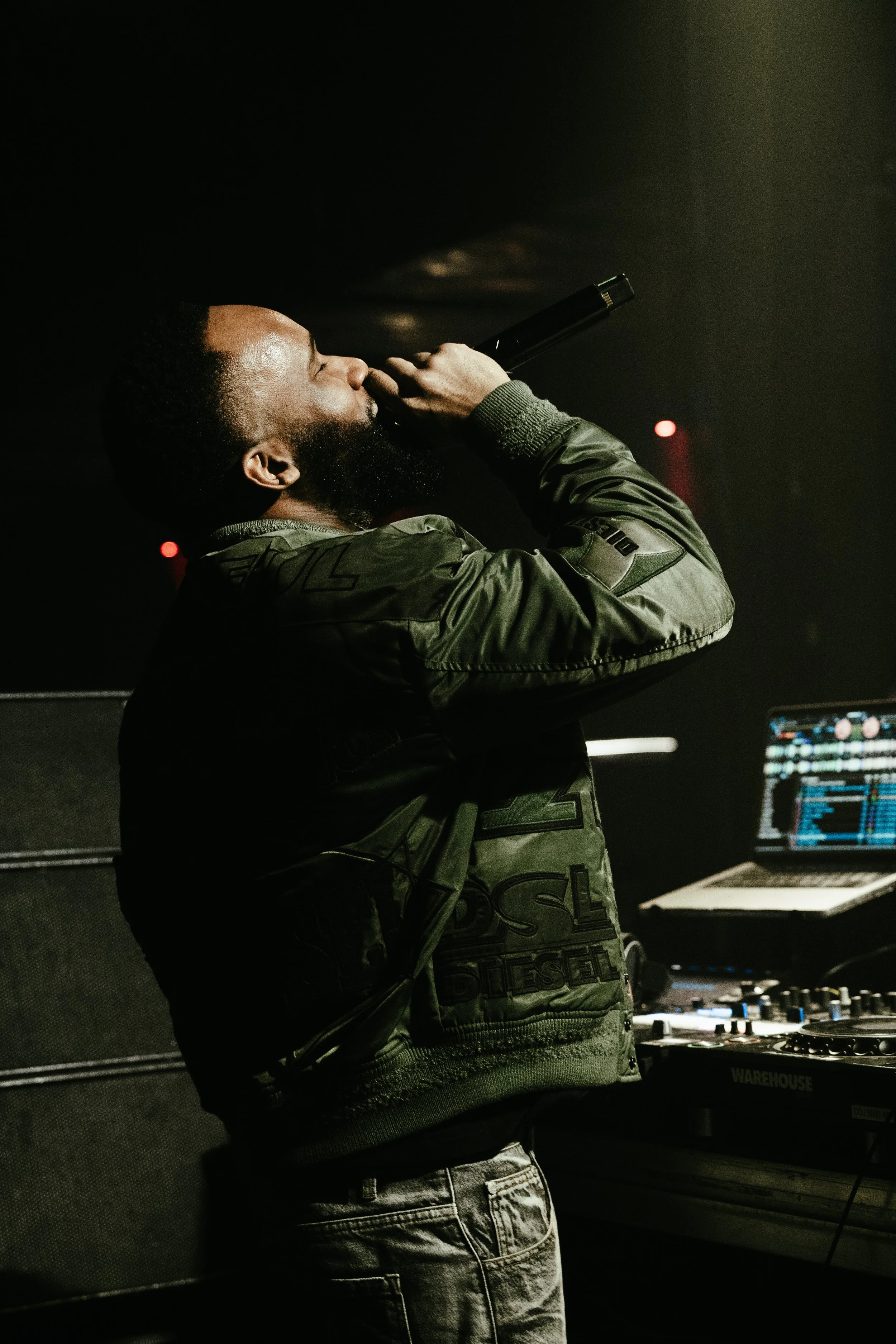 Un DJ ou un artiste en train de chanter ou de rapper lors d'une performance dans un club ou un concert, avec un ordinateur portable à proximité.
