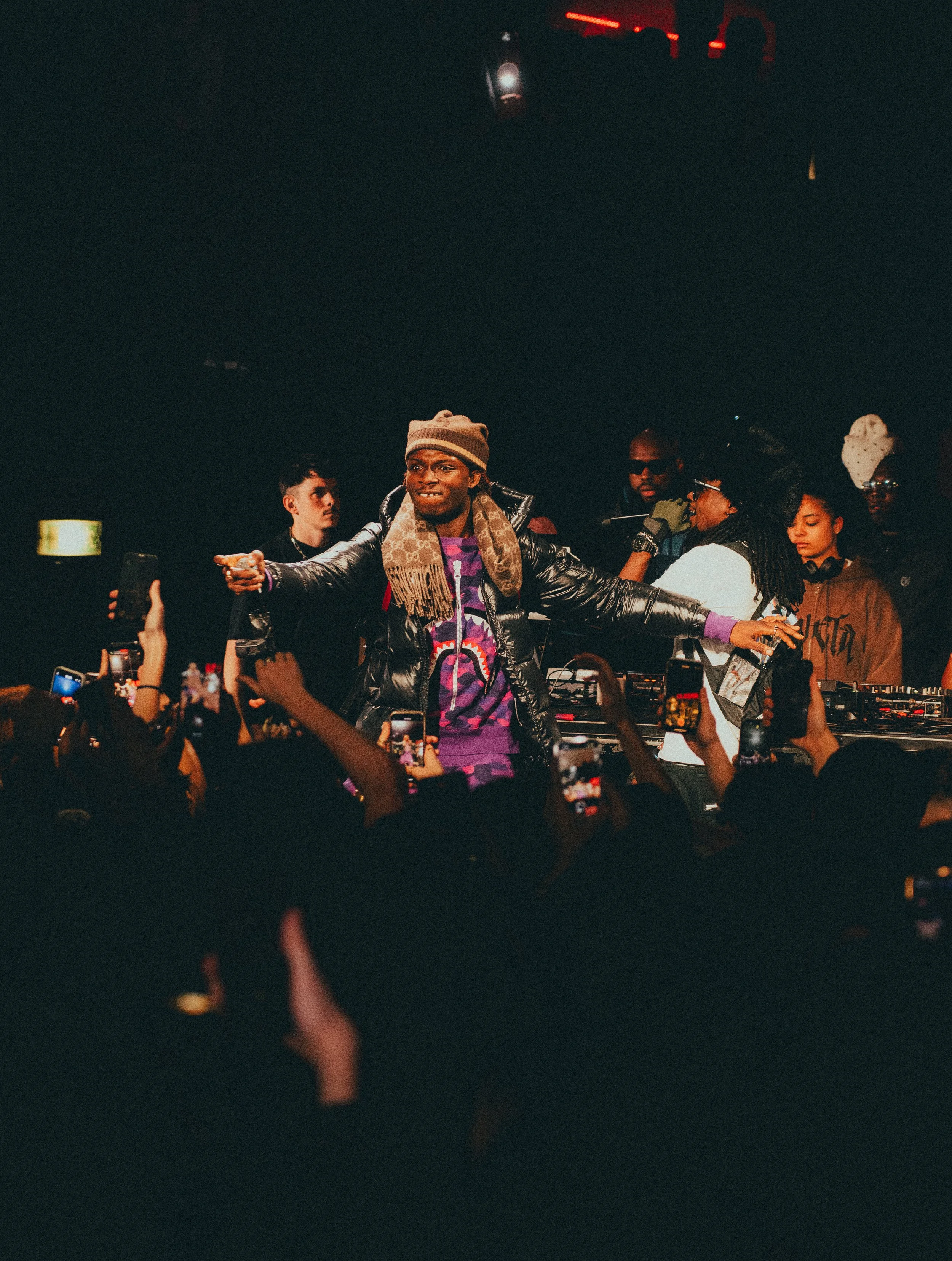 DJ performe sur scène lors d'un concert avec un public qui prend des photos et des vidéos.