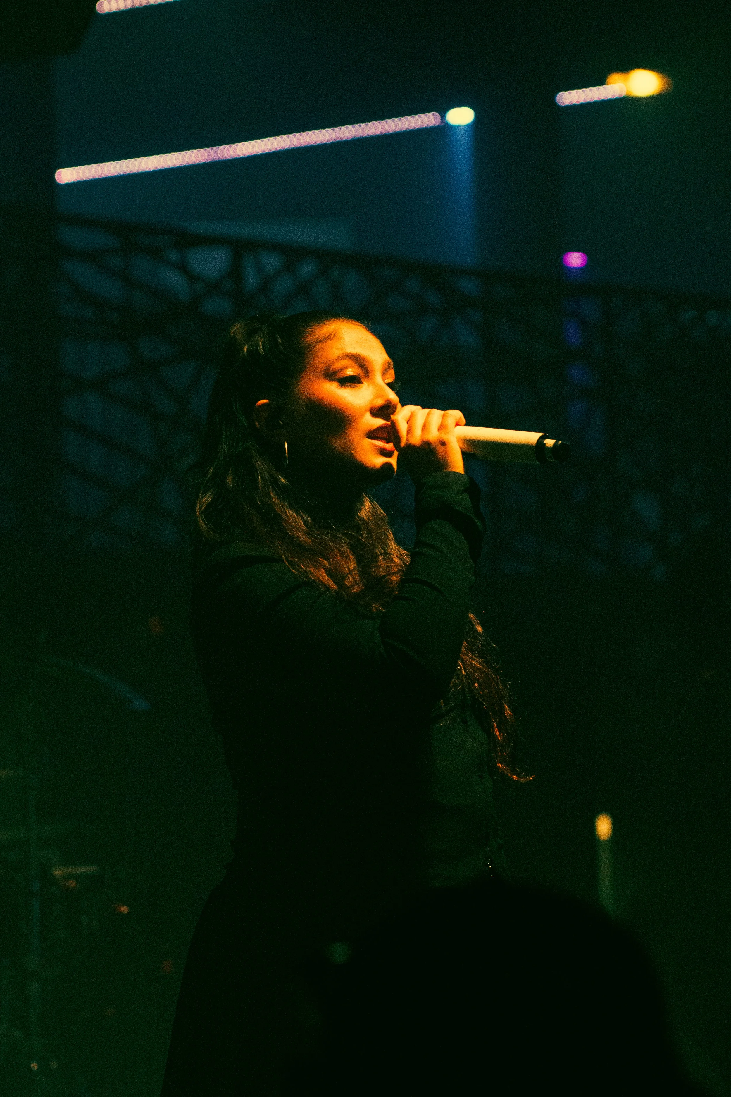 Une femme chante dans un micro lors d'un spectacle sur scène avec des éclairages de couleurs vives en arrière-plan.