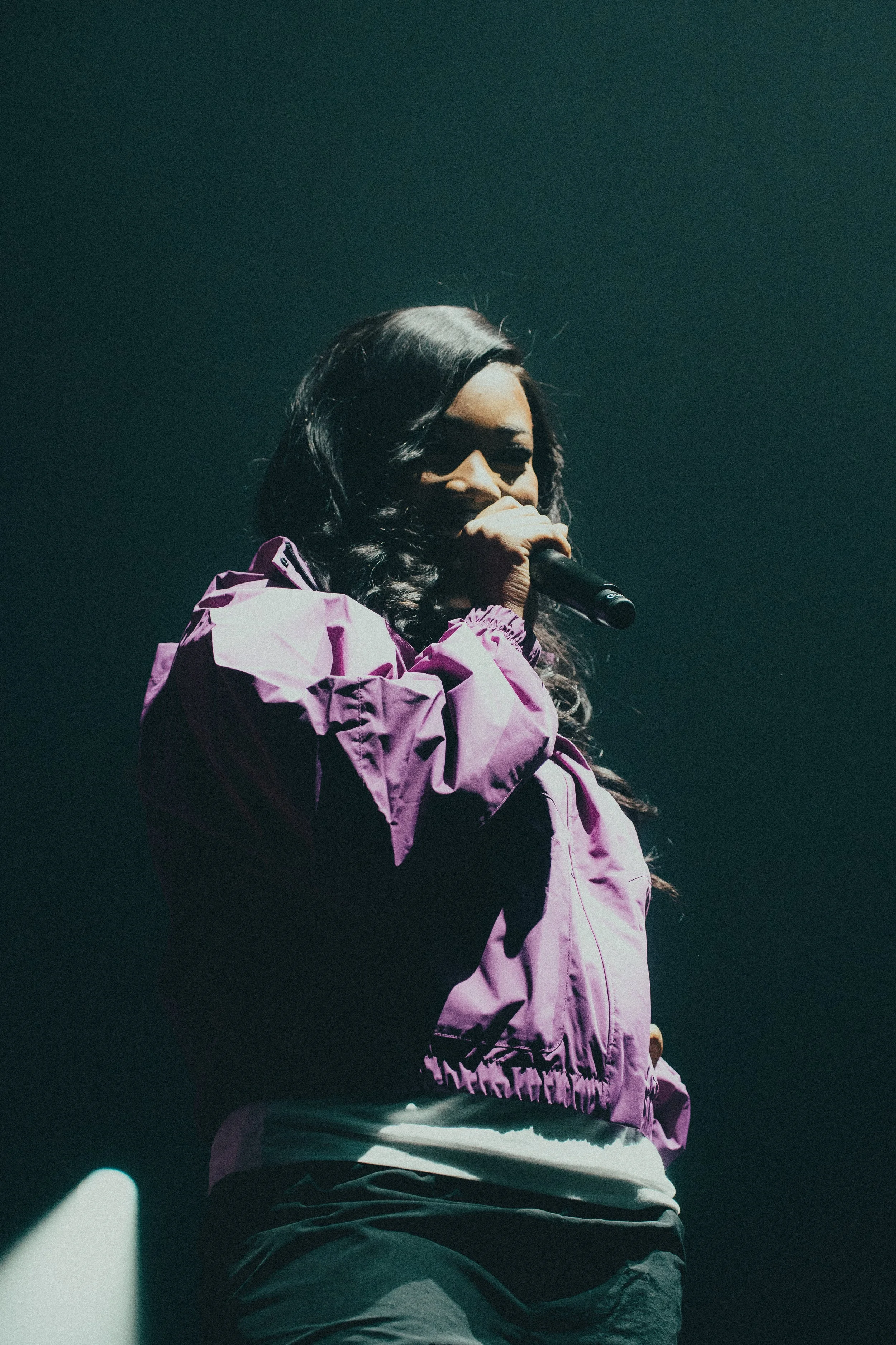 Femme chantant avec un micro sur scène, portant une veste violette
