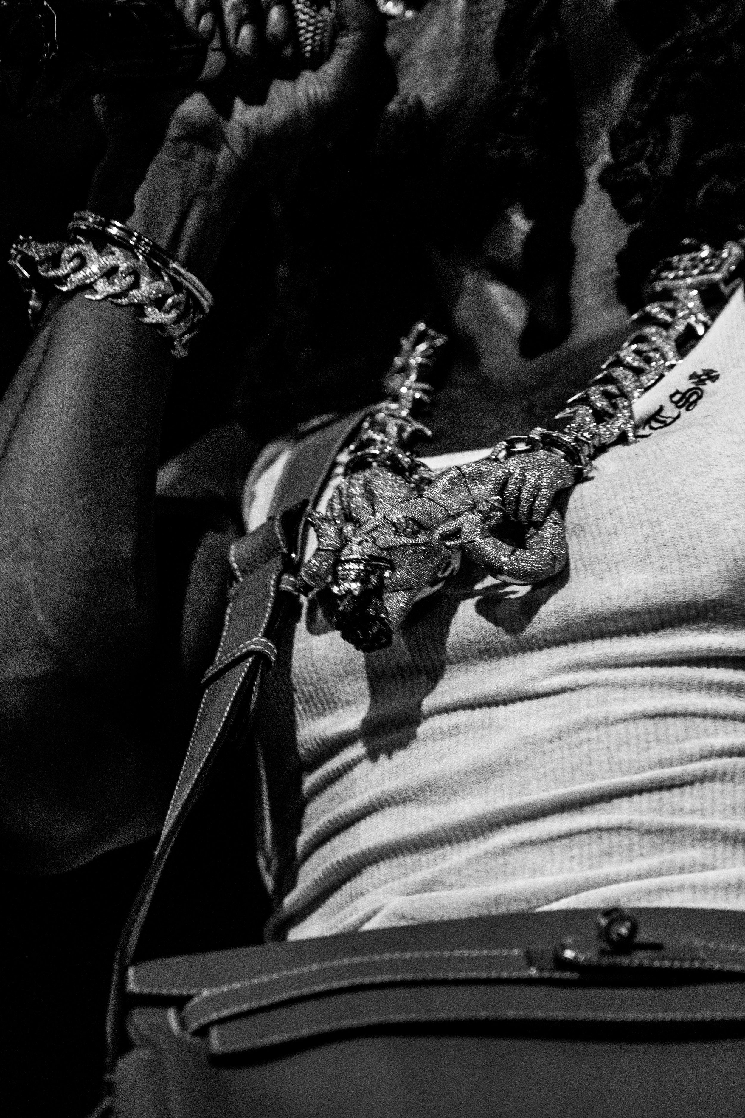 Gros plan de plusieurs bijoux en or et en diamant, notamment une chaîne et une montre, et une personne portant un t-shirt rayé, dans un style urbain.