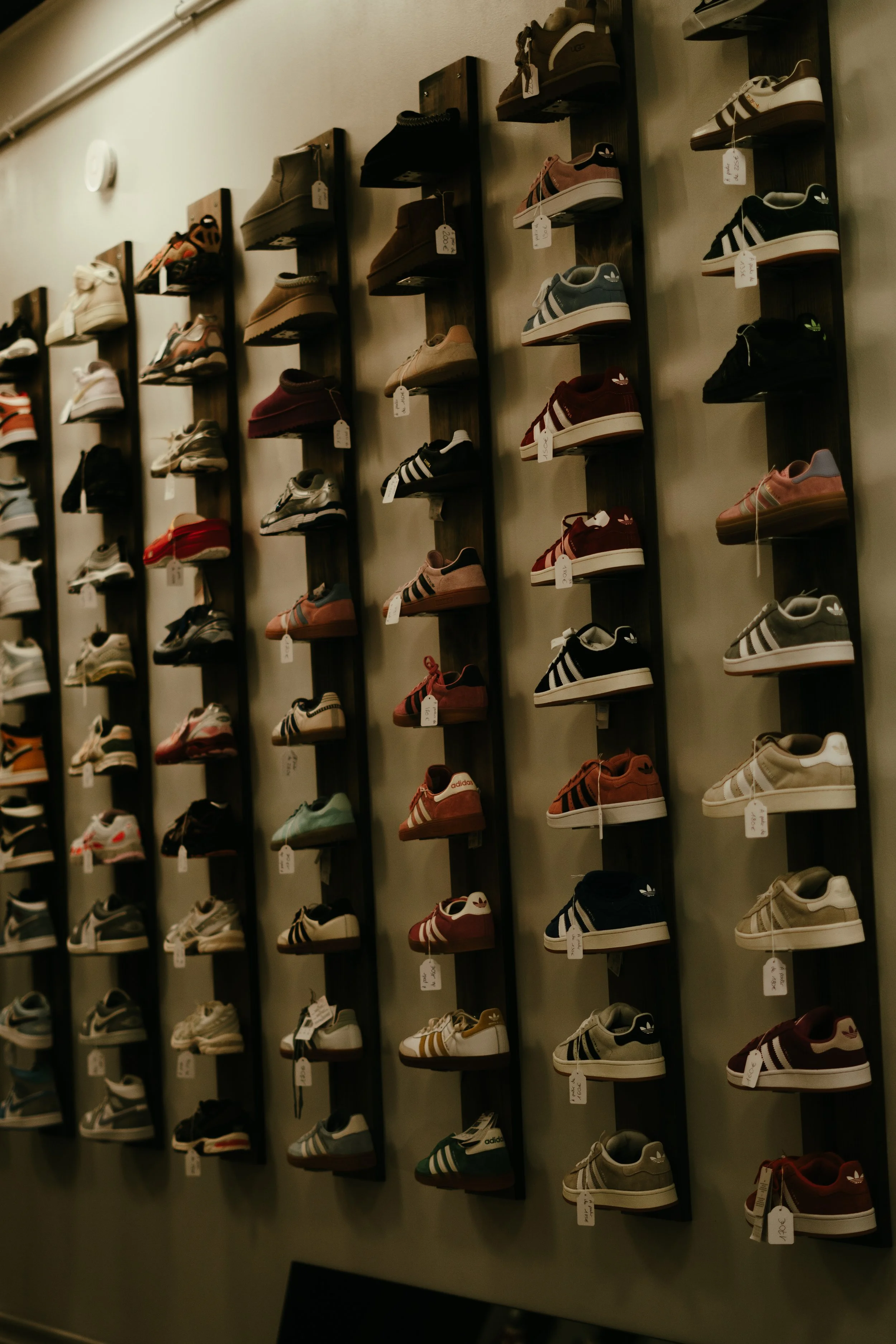 Une murale avec plusieurs étagères en bois fixées verticalement, affichant des chaussures de sport de différentes couleurs et marques dans un magasin.