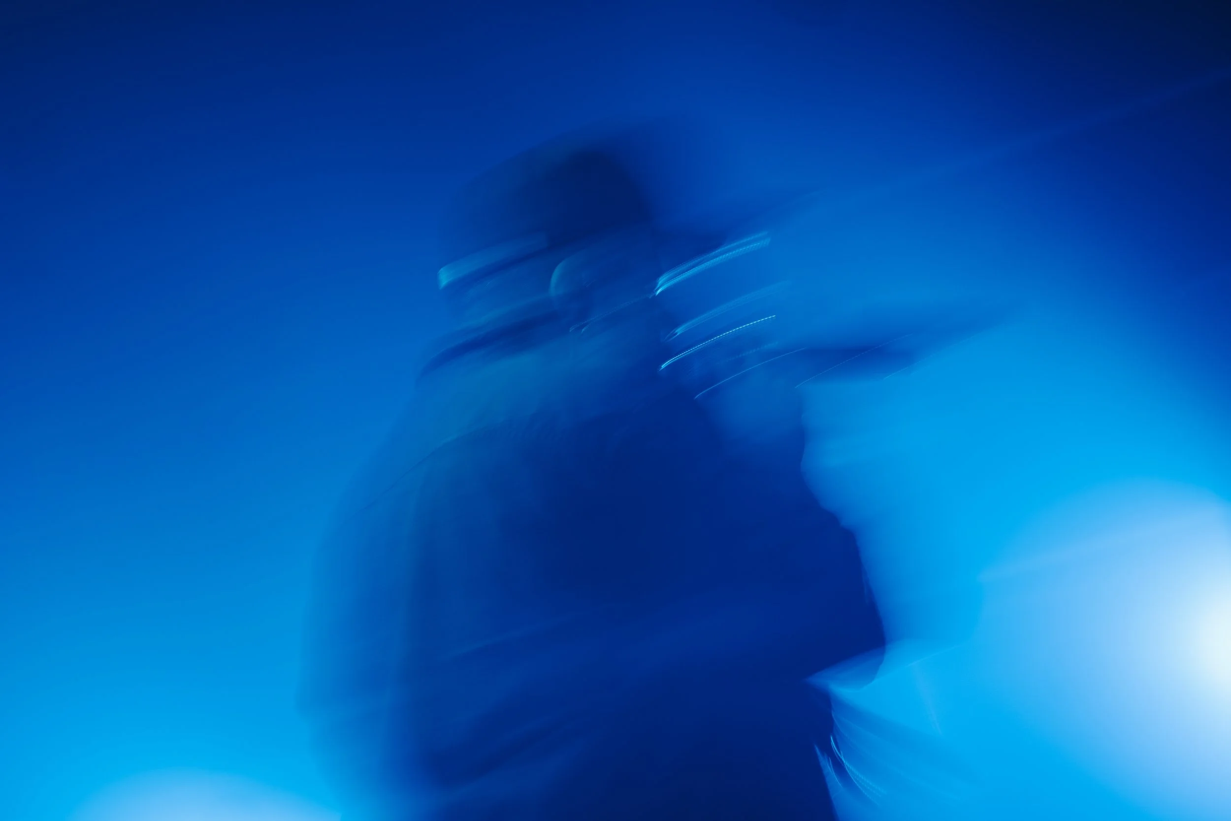 Une silhouette floue d'une personne portant des lunettes de sécurité dans un environnement sombre, avec un éclairage bleu.