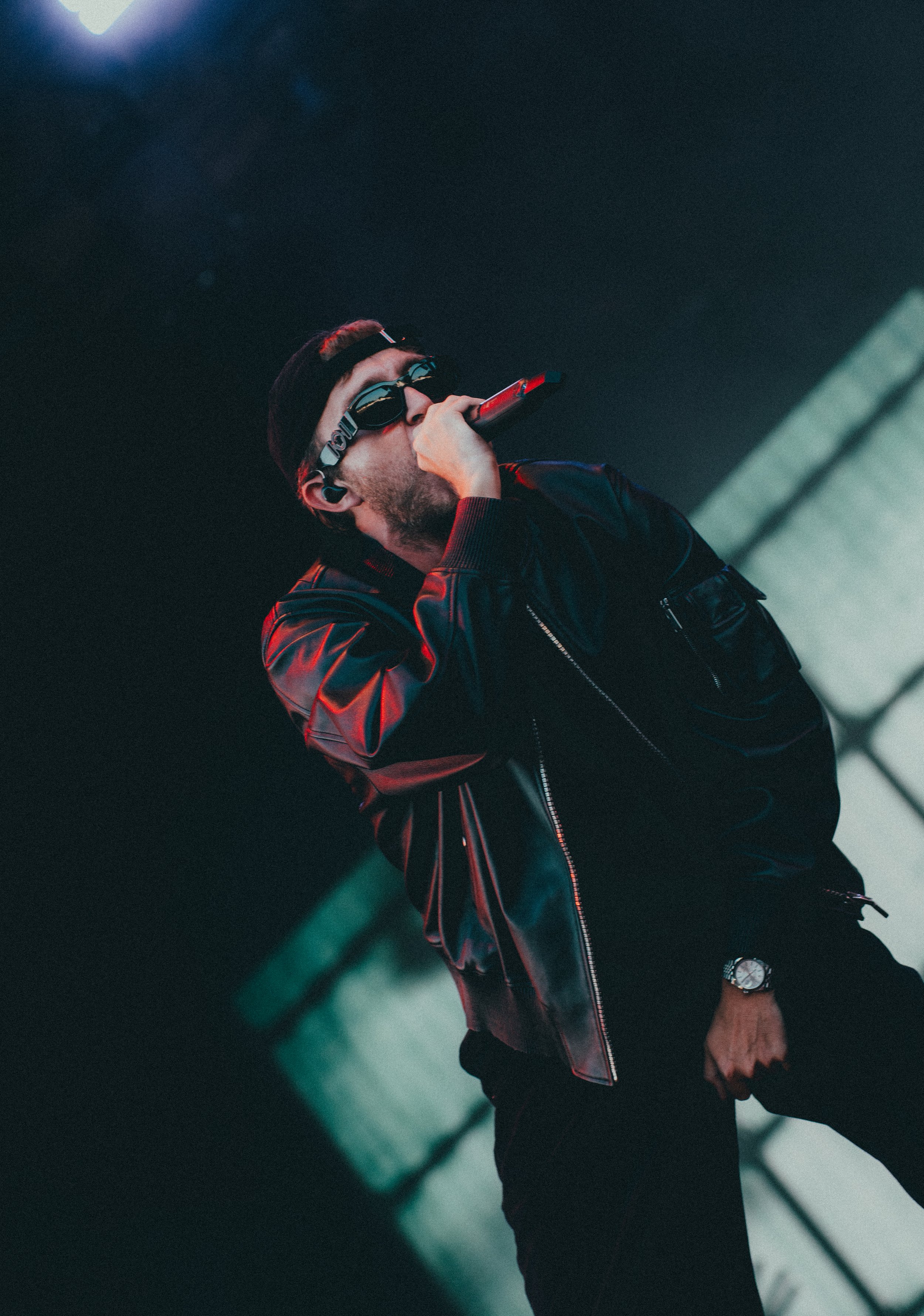 Un homme portant des lunettes de soleil noires et un casque écoute de la musique avec un microphone à la main, portant une veste en cuir noir
