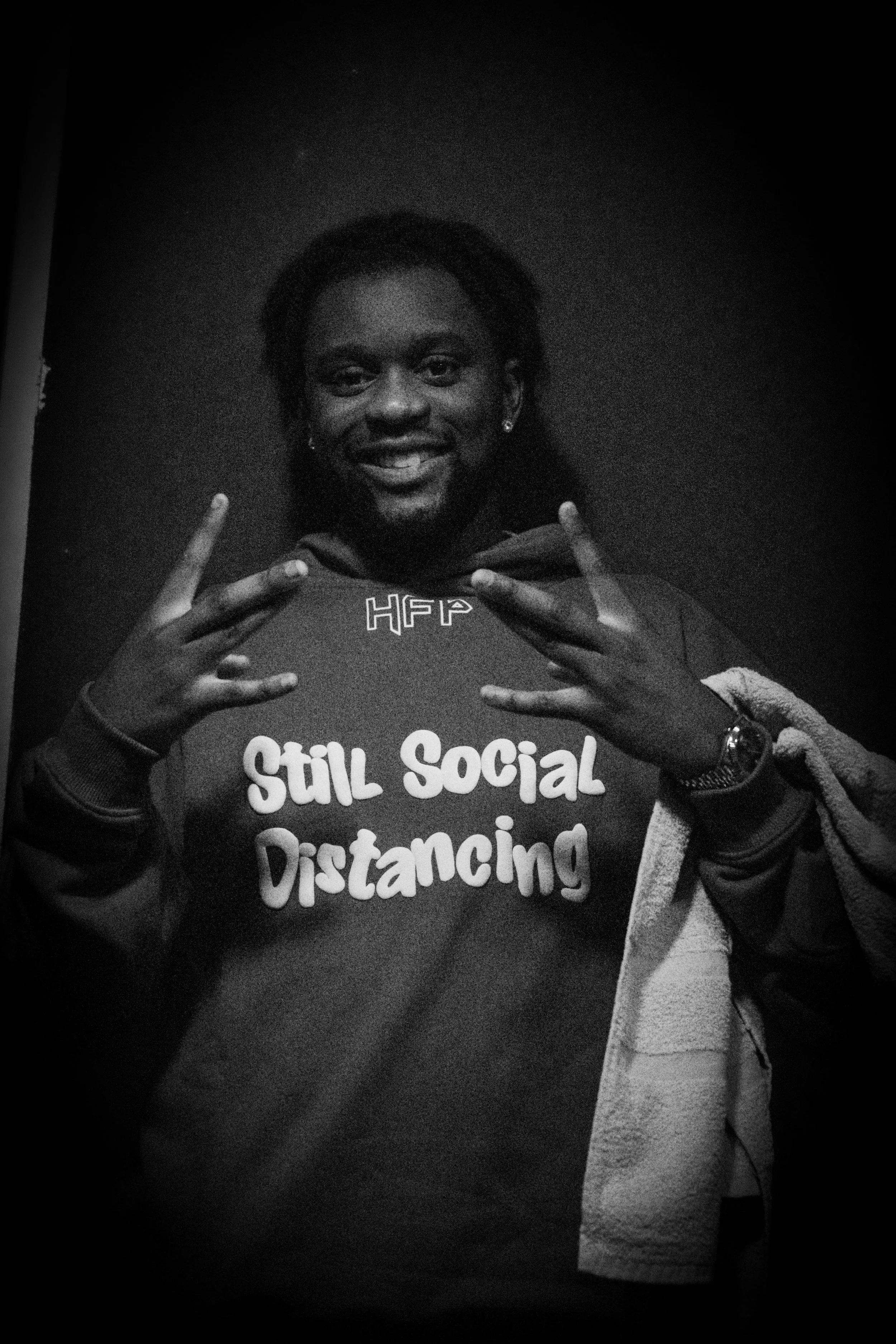 Jeune homme souriant portant un sweat-shirt avec l'inscription 'Still Social Distancing'