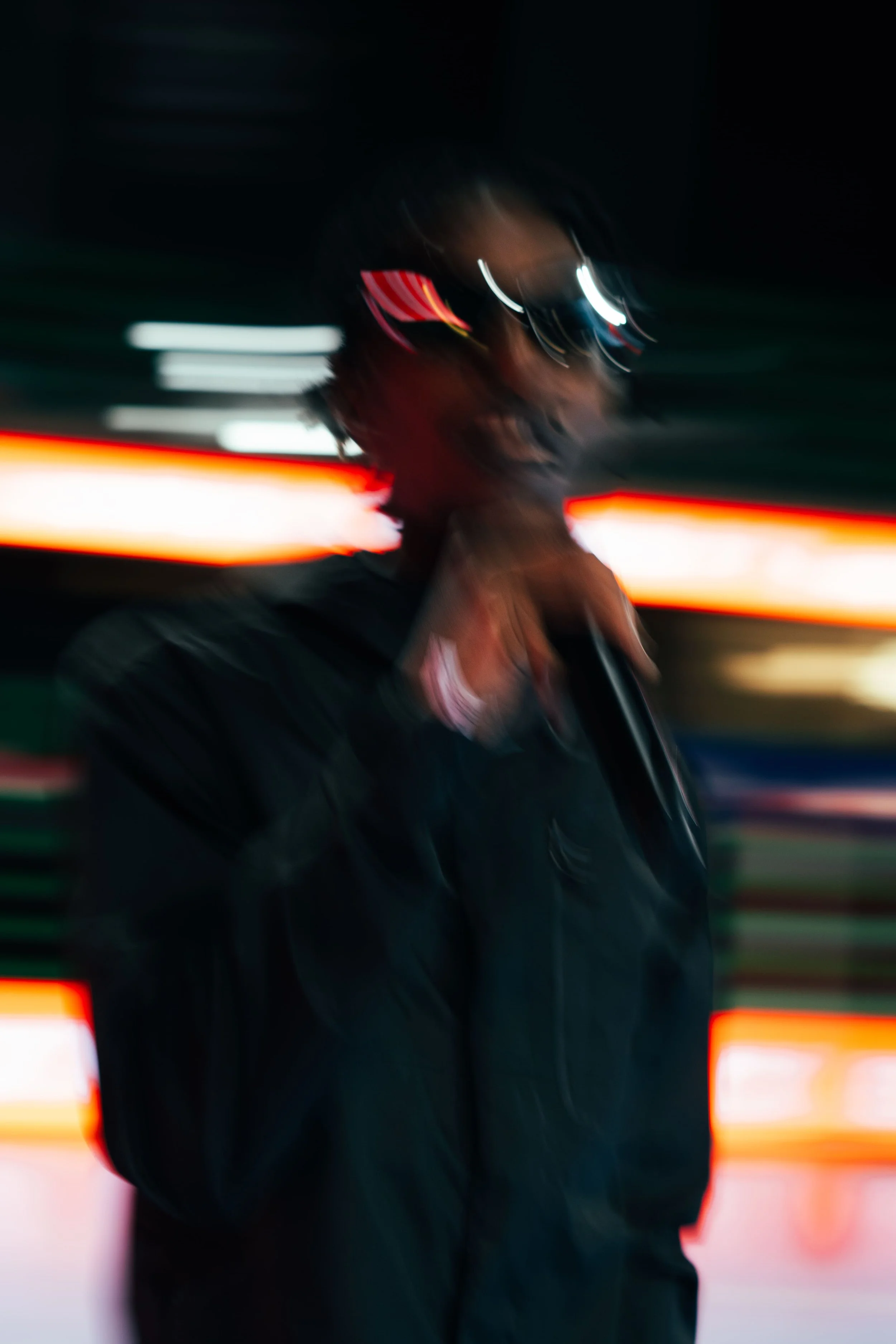 Personne souriante portant des lunettes de soleil, avec un fond coloré de lumières nocturnes floues.