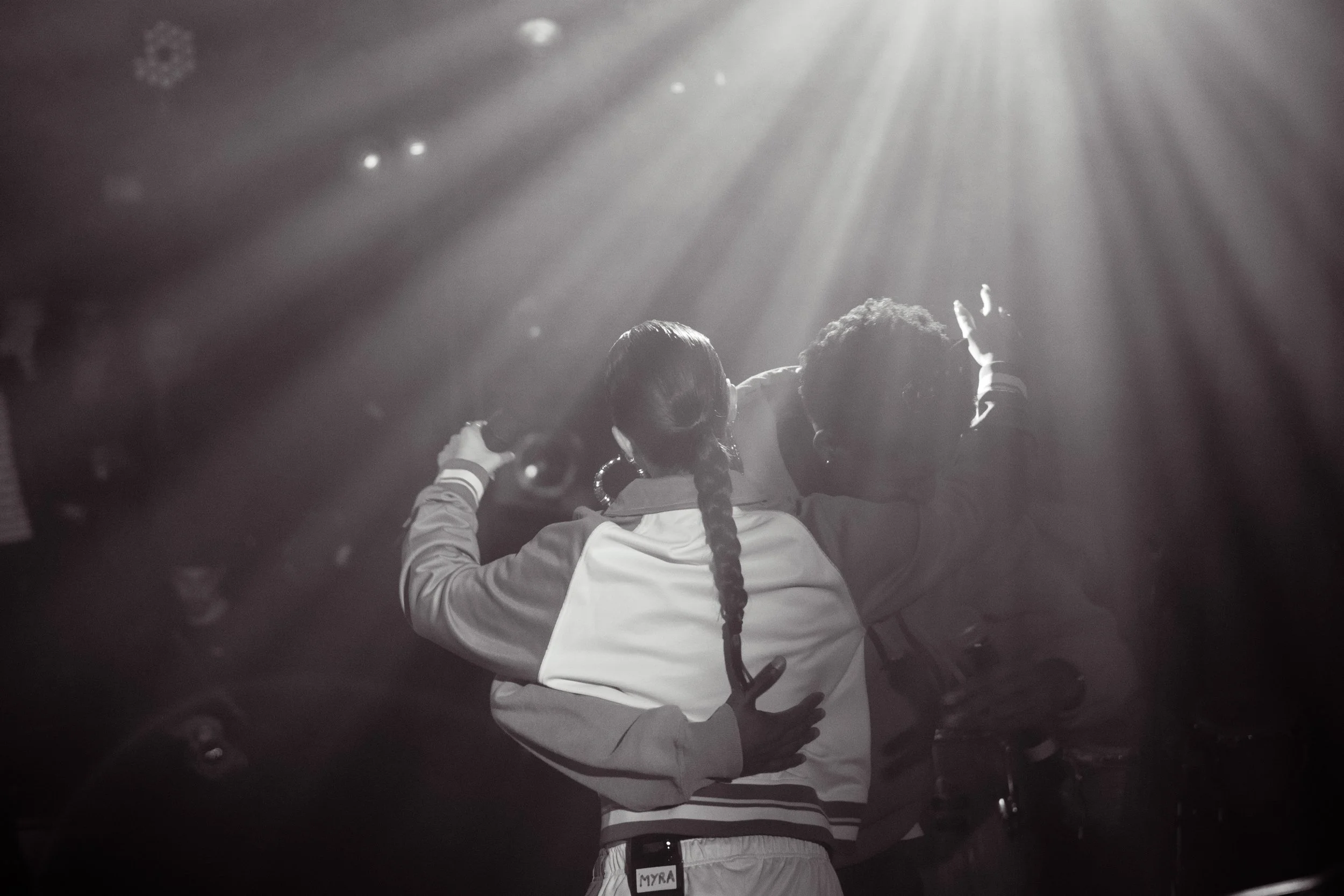 Deux personnes dansent et s'enlacent sous un éclairage de scène, vue de derrière, dans une ambiance de concert ou de fête.