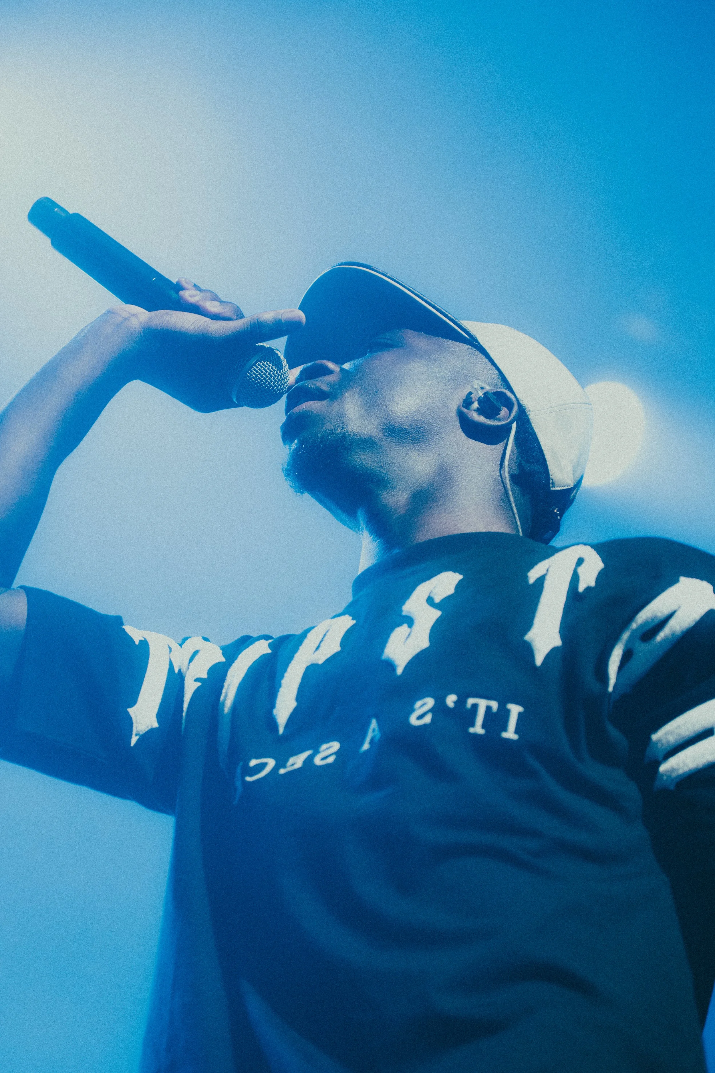 Un homme chante dans un microphone, portant une casquette et un casque d'écoute