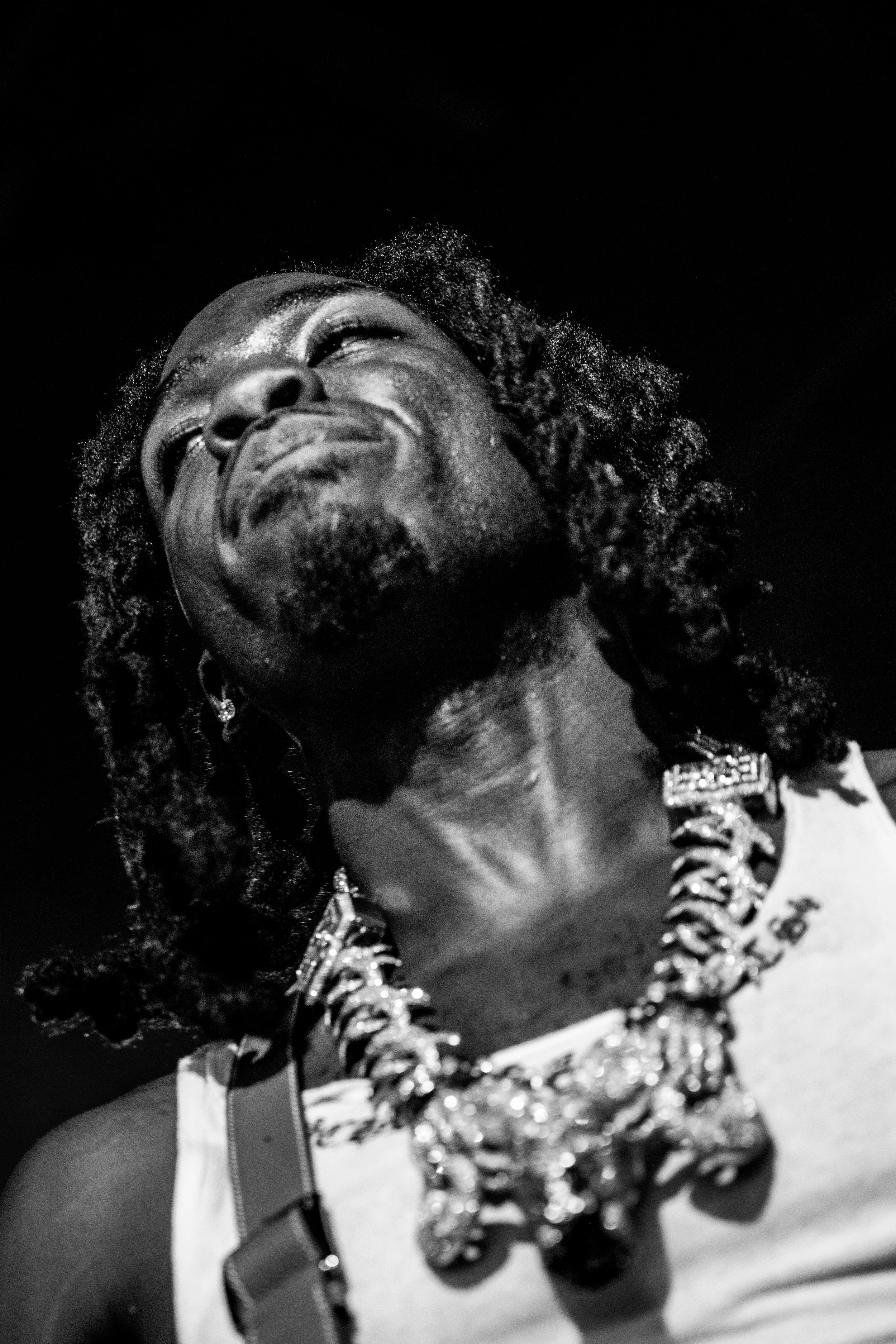 Portrait en noir et blanc d'une femme avec des dreadlocks, portant un collier volumineux, avec un regard levé et une expression d'émotion.