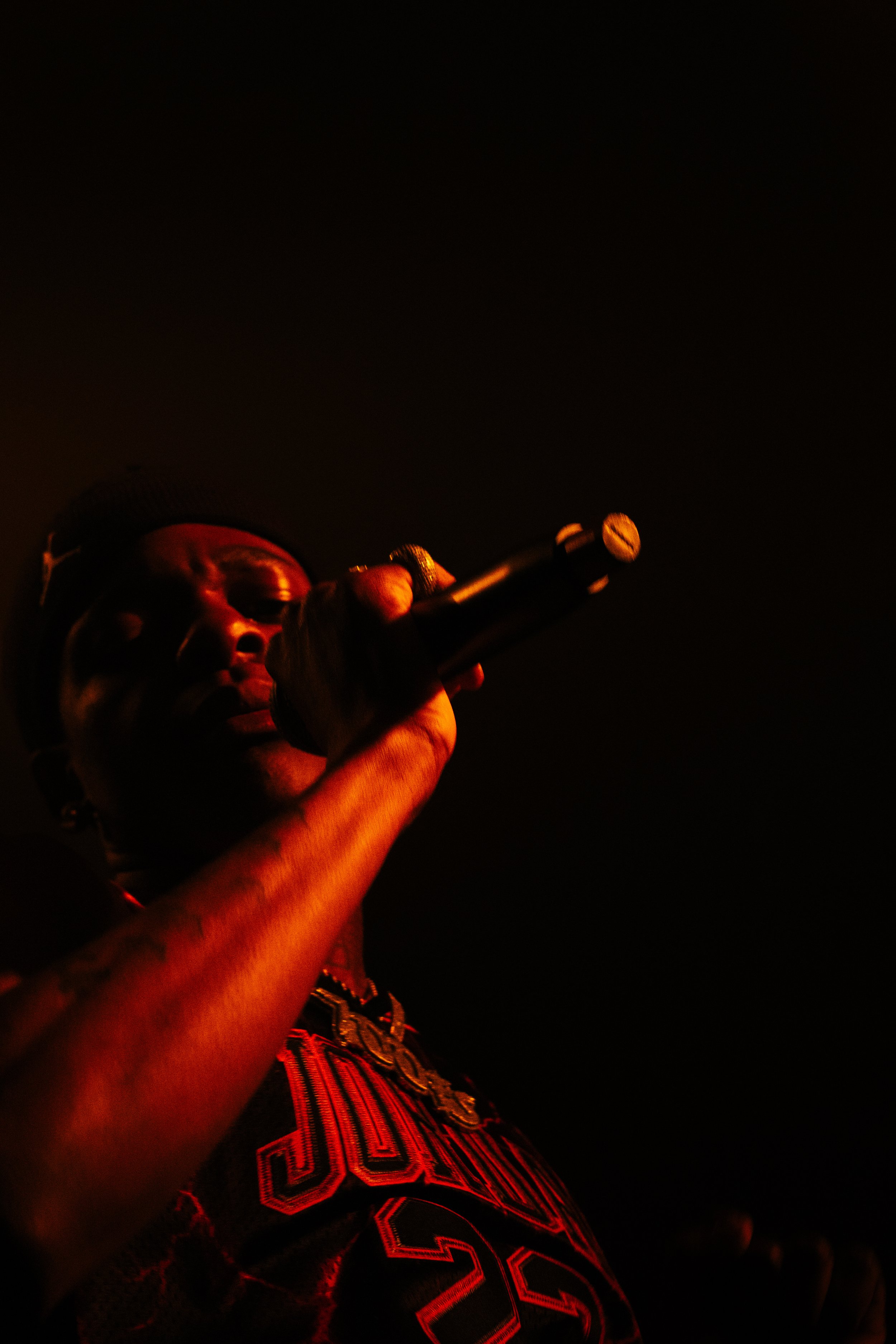 Une personne tenant un microphone, éclairée par une lumière rouge sur un fond sombre.