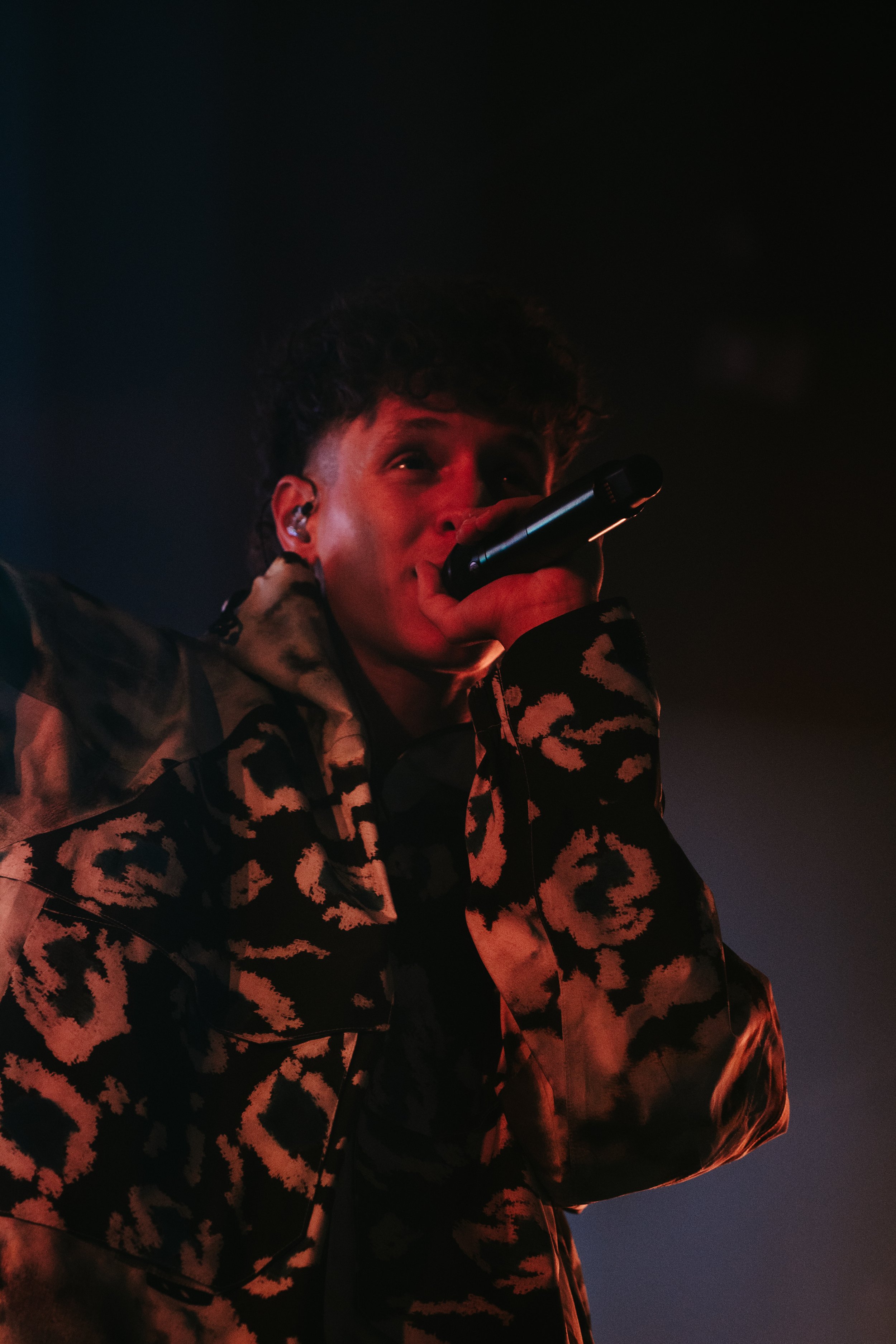 Un jeune homme chante en utilisant un microphone lors d'un concert, portant un vêtement à motif camouflage.