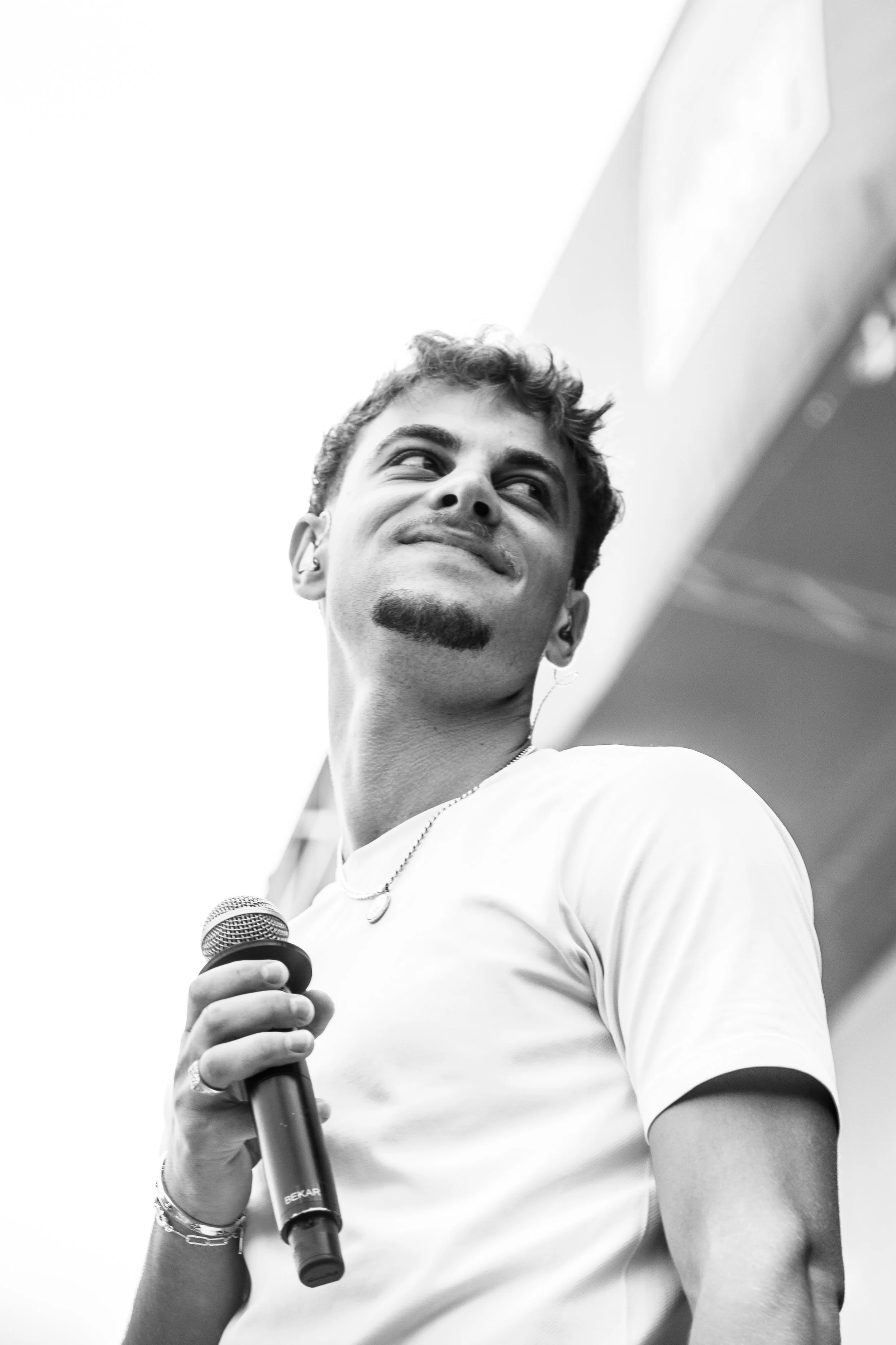Un homme souriant tenant un micro lors d’un événement en plein air, en noir et blanc.