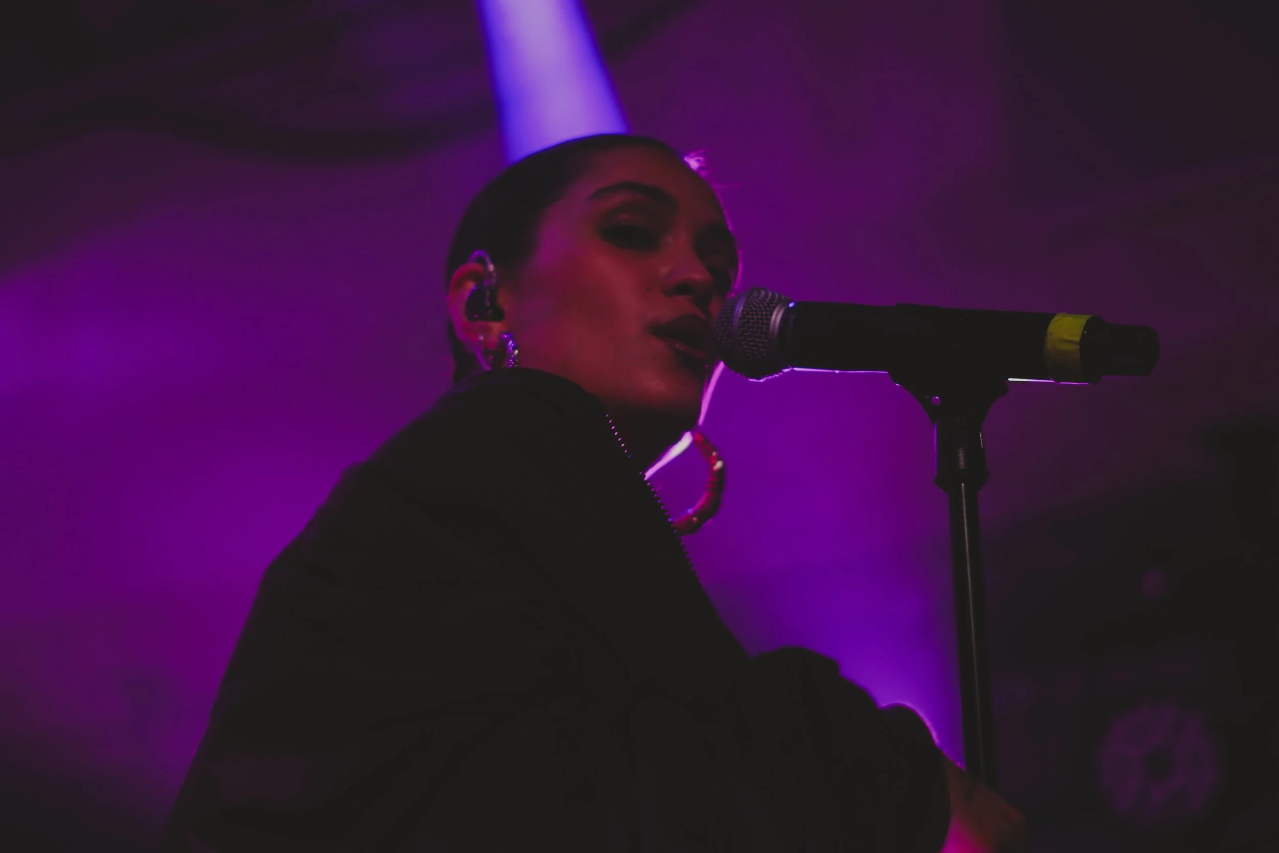 Une femme chante dans un micro lors d'une performance sous un éclairage violet