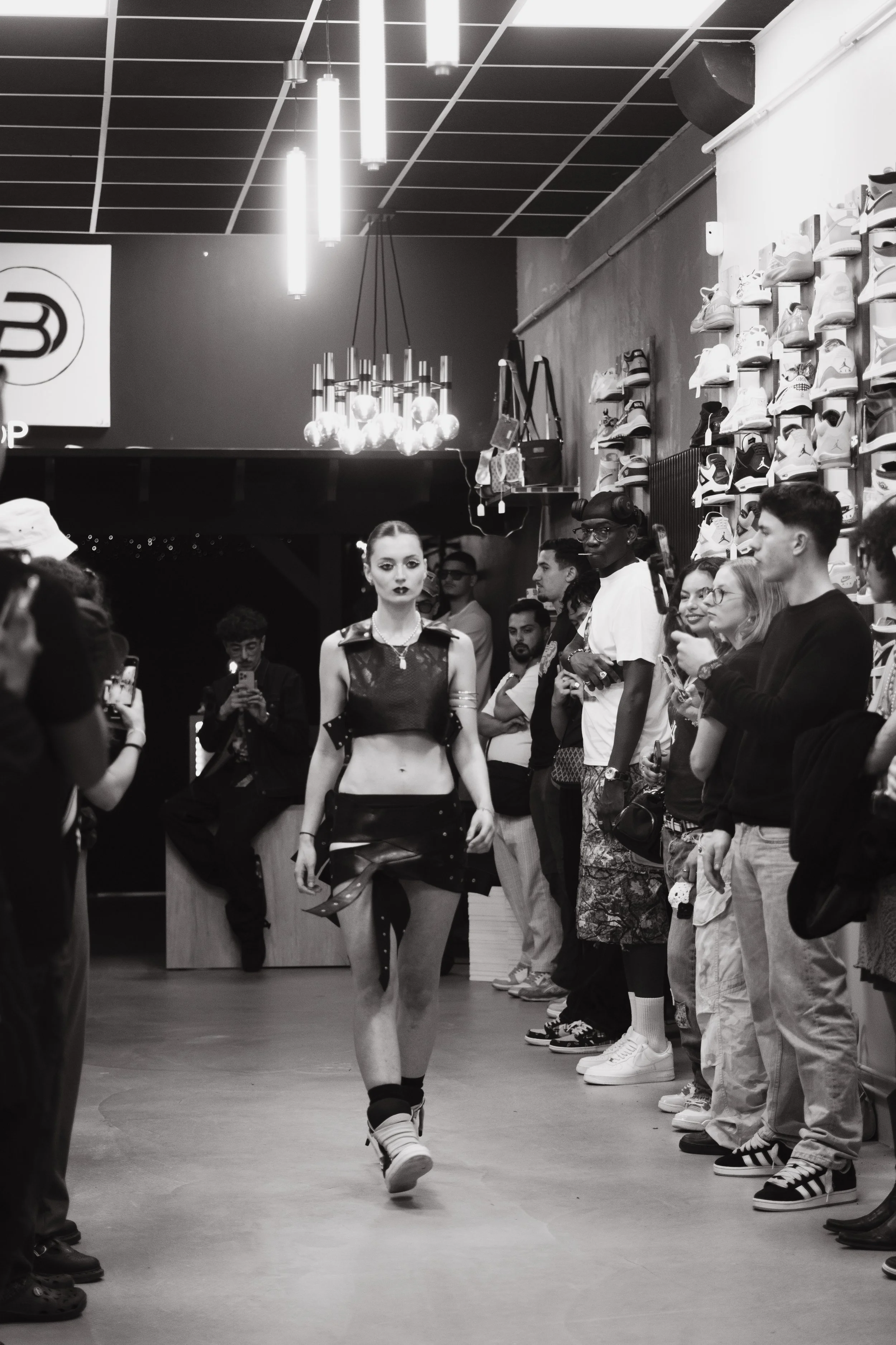 Une femme marche sur un podium lors d'un défilé de mode dans un magasin de chaussures, entourée de spectateurs.