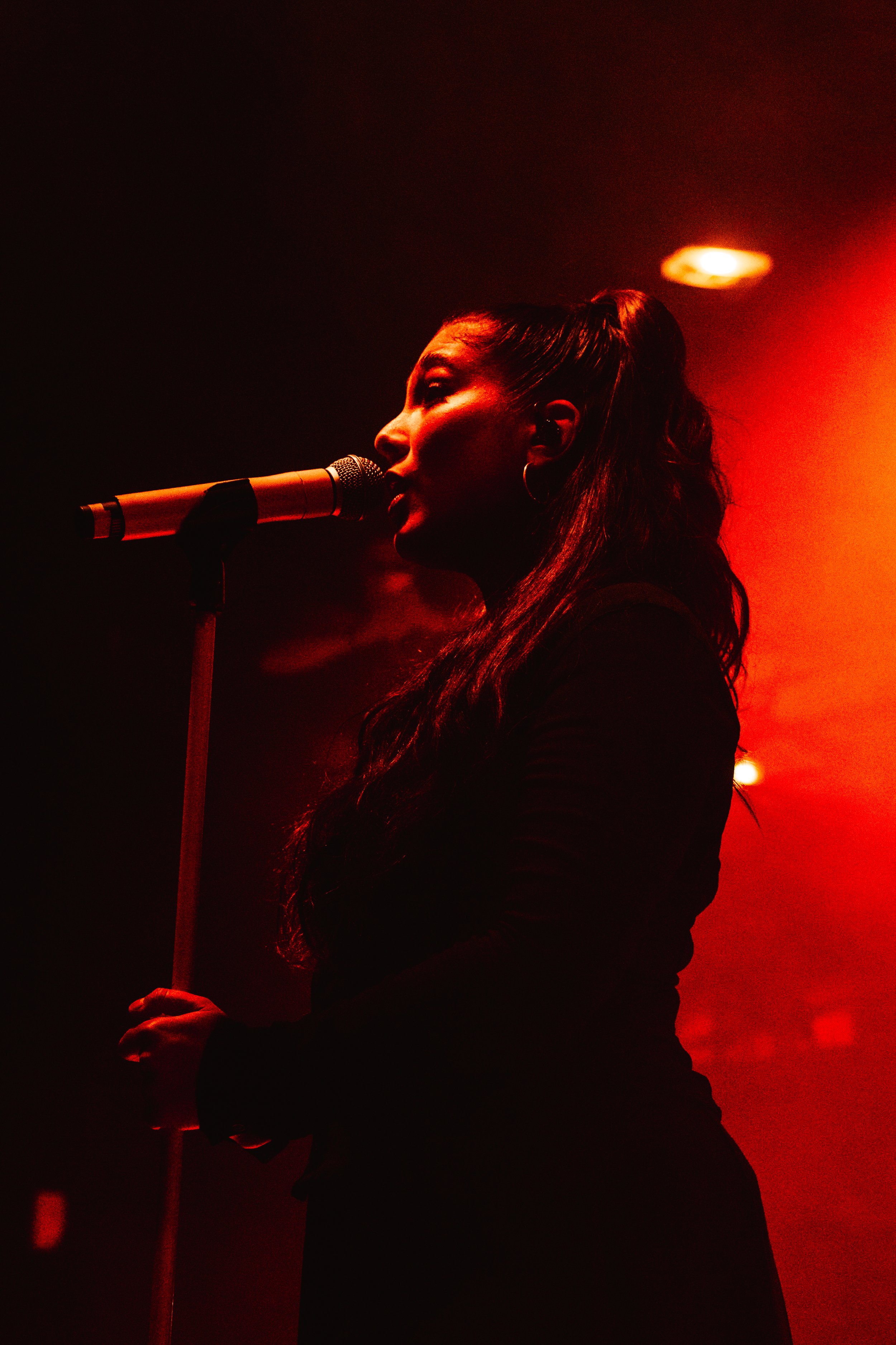 Une femme chante avec un micro dans une ambiance sombre et rougeâtre.