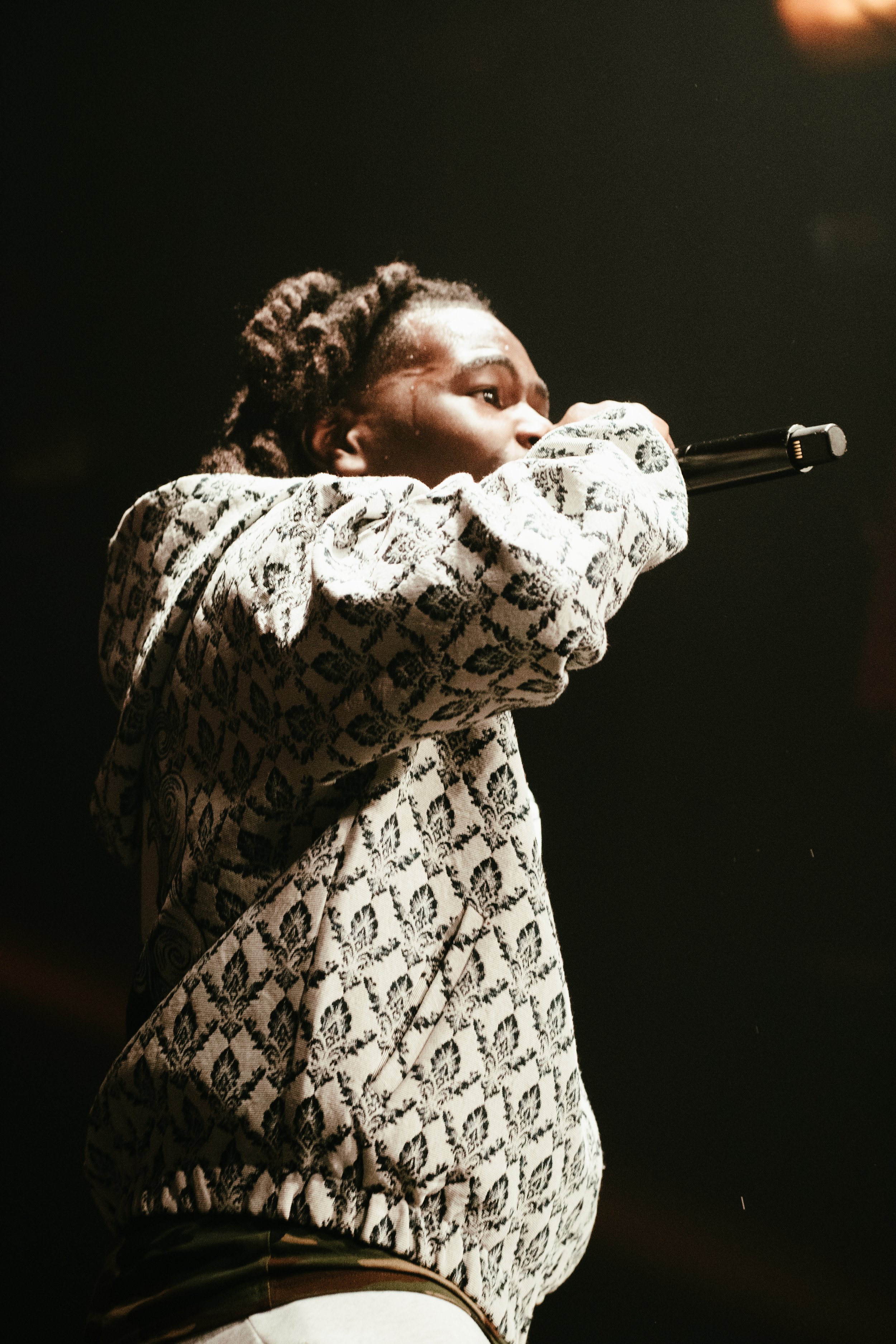 Un homme chante ou parle dans un microphone dans une ambiance sombre.