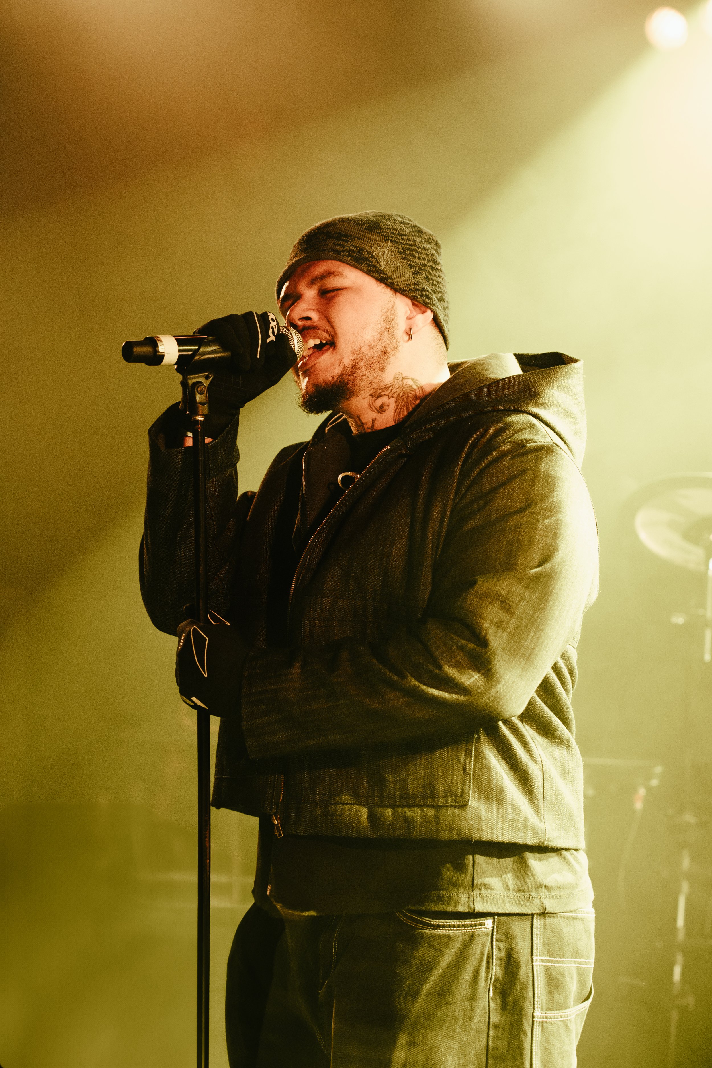 Un homme chante dans un micro lors d'une performance musicale, avec un éclairage jaune autour.