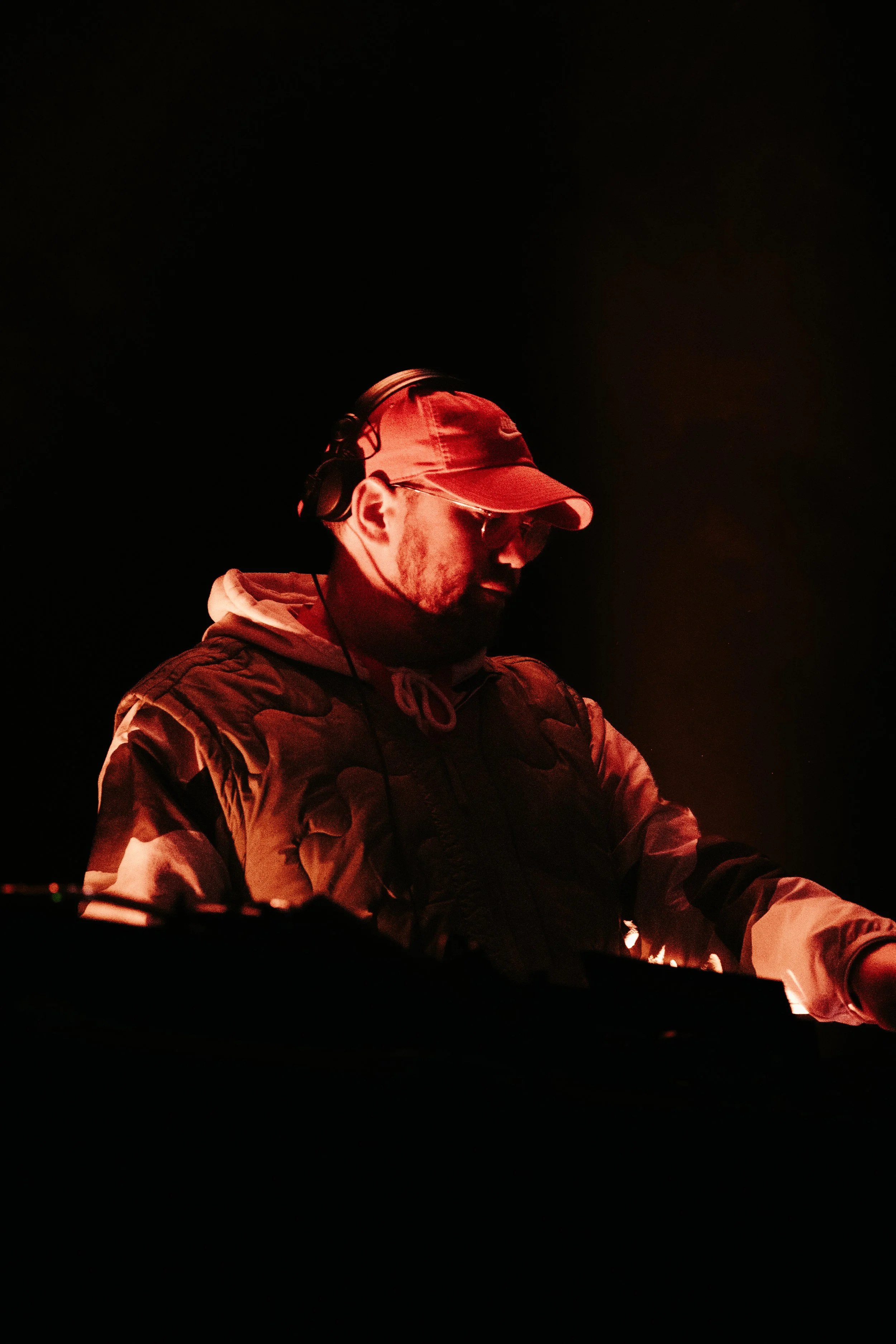 DJ portant un casque et des lunettes, éclairé par une lumière rouge dans l'obscurité