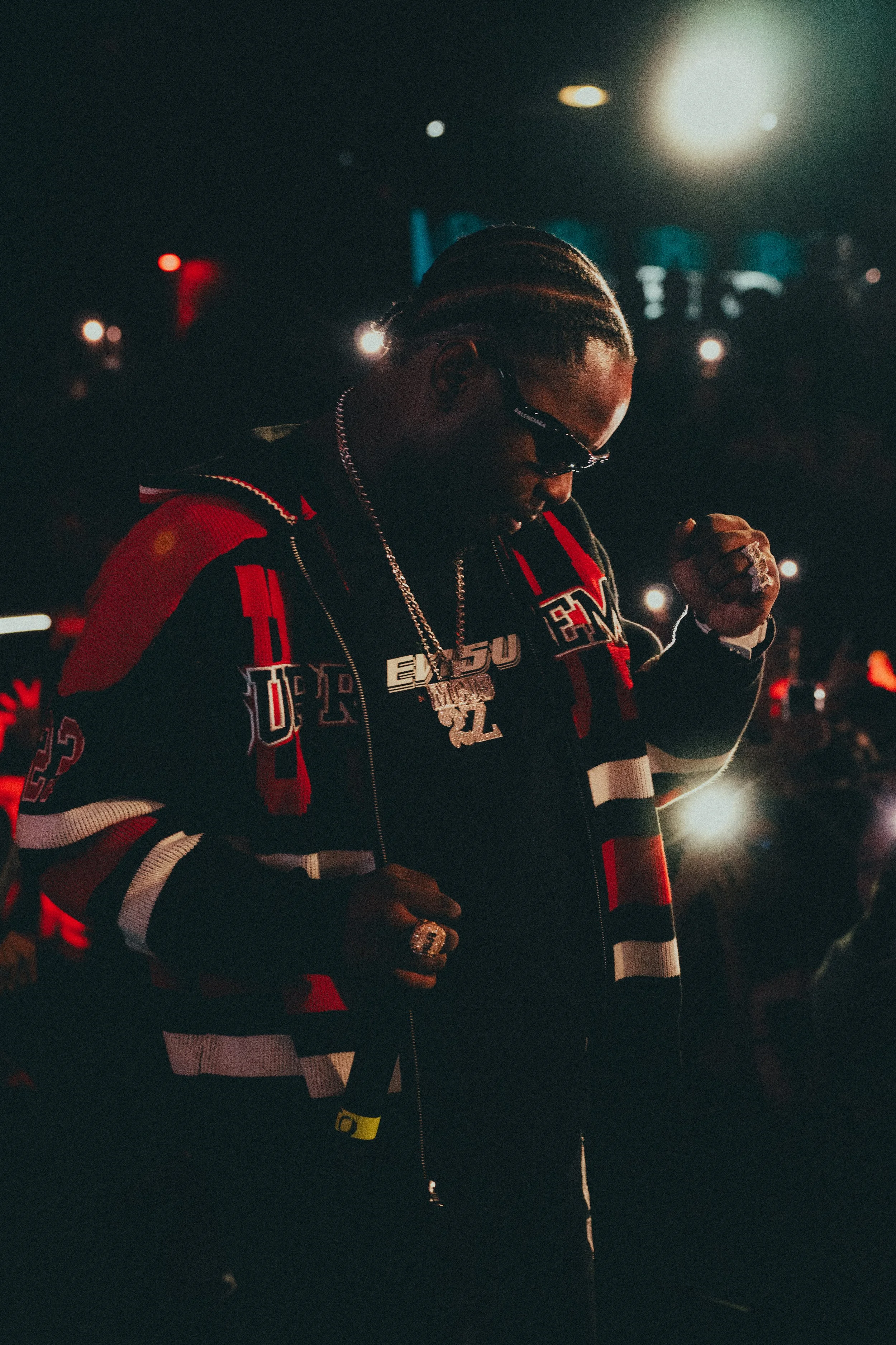 Un homme portant des vêtements décontractés, des bijoux et portant des lunettes de soleil, avec un éclairage de nuit.