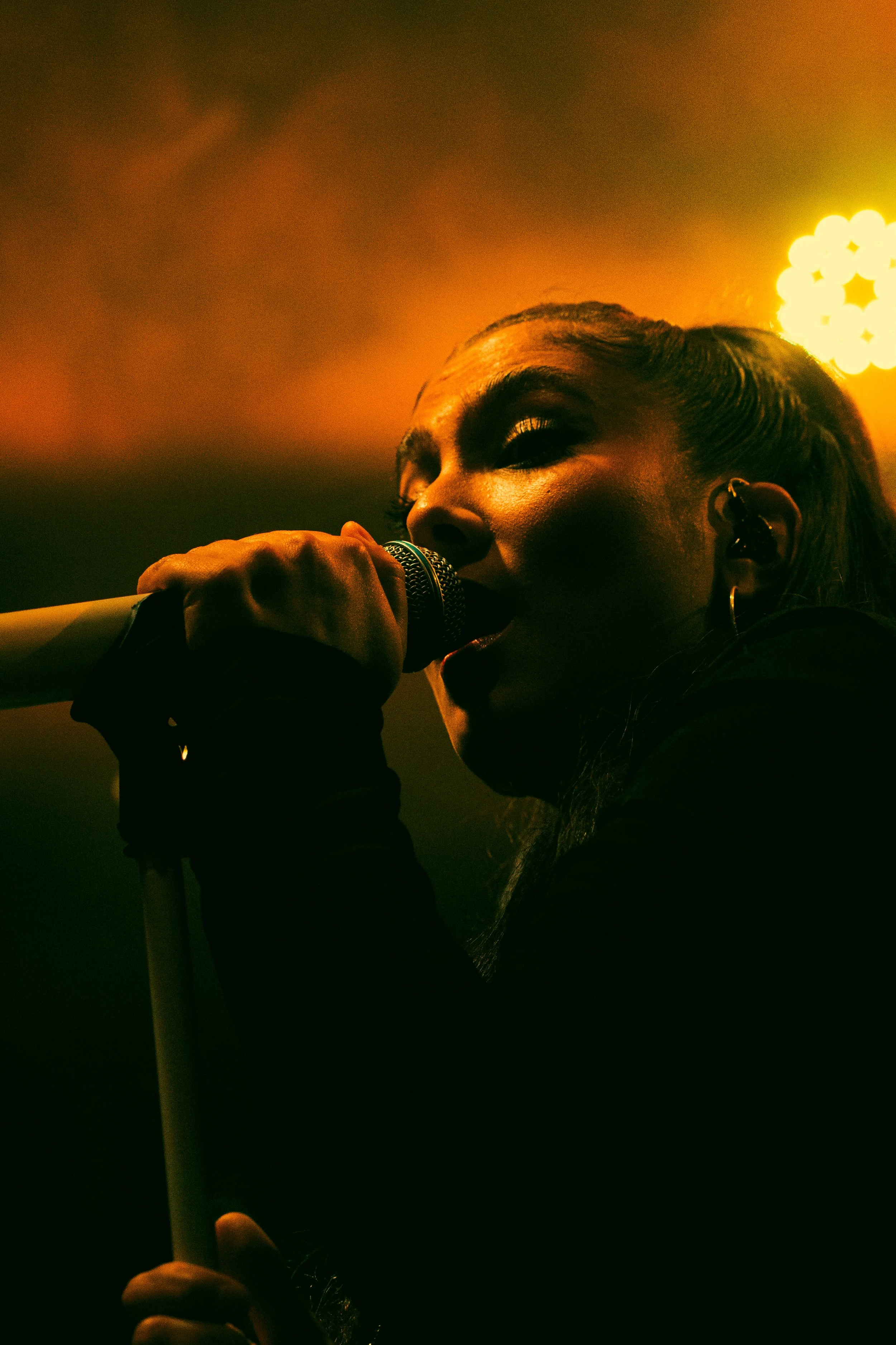 Une femme chantant dans un micro lors d'une performance, avec un éclairage chaud en fond.