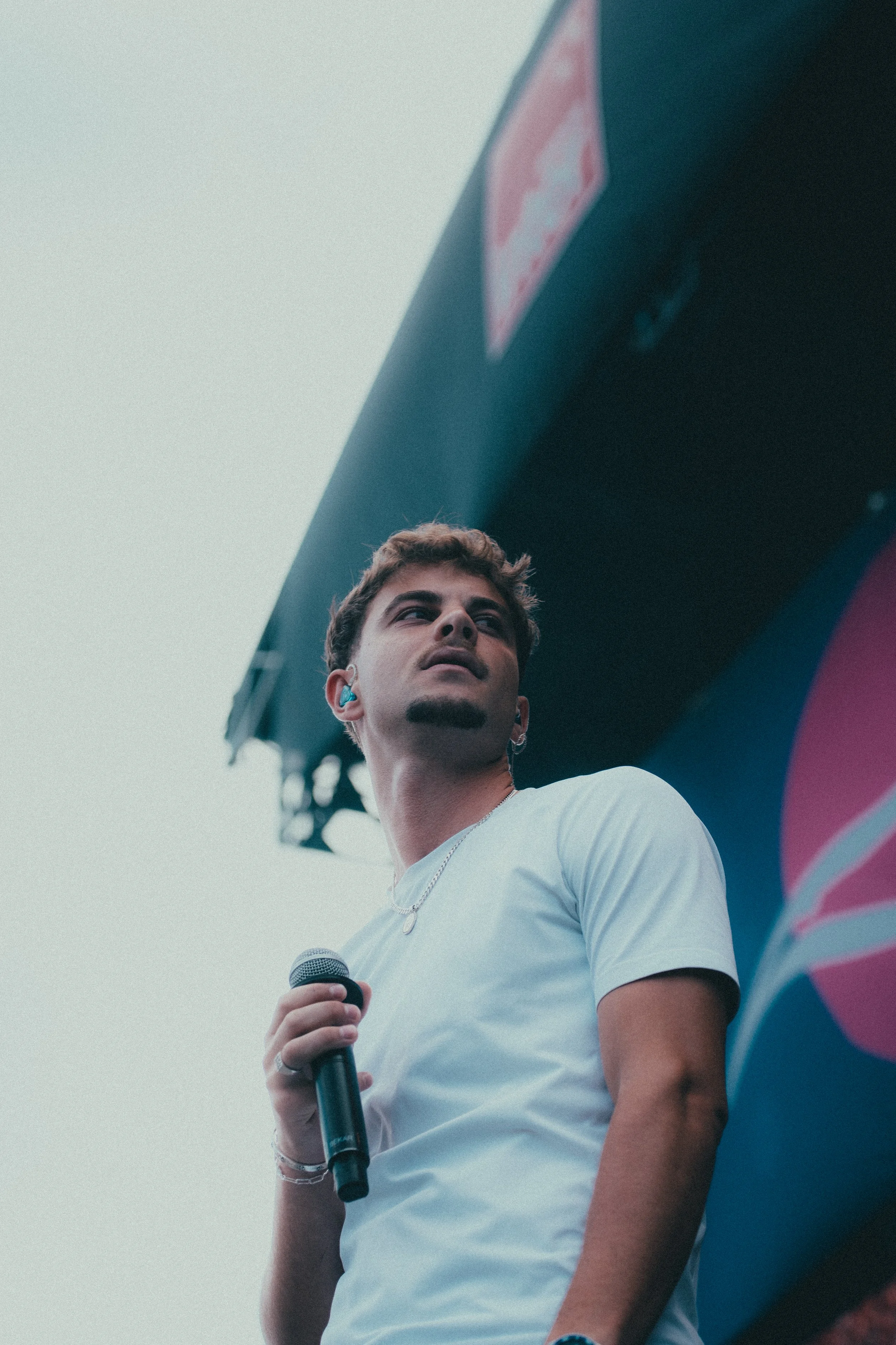 Un jeune homme tenant un micro, vu de dessous, en pleine performance ou discours, avec un fond d'écran de scène ou grand écran