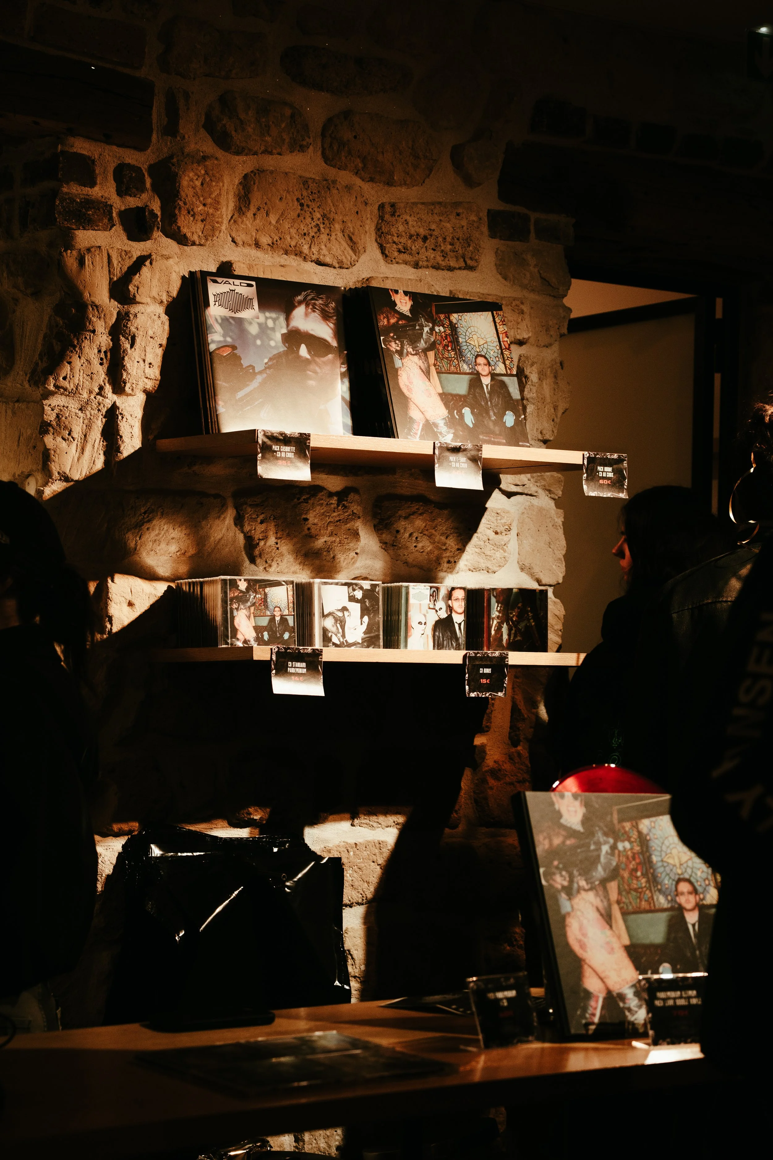 Vente de vinyles dans une boutique, avec des clients regardant des disques sur des étagères en pierre, ambiance chaleureuse avec éclairage tamisé.