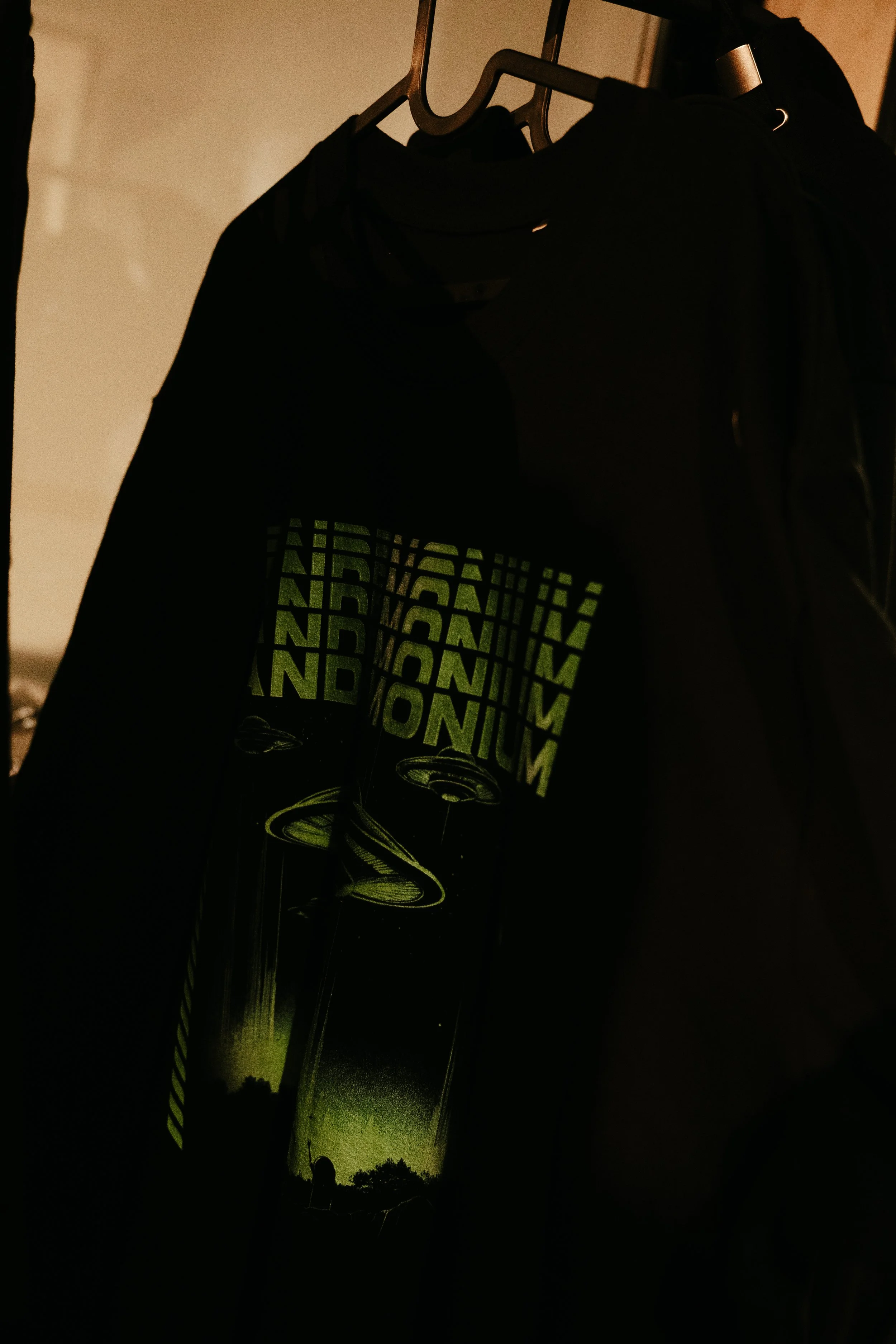 Vêtements noirs suspendus sur des cintres dans une pièce sombre, avec un design lumineux représentant des cercles et un texte vert indiquant 'MAGNUM'.